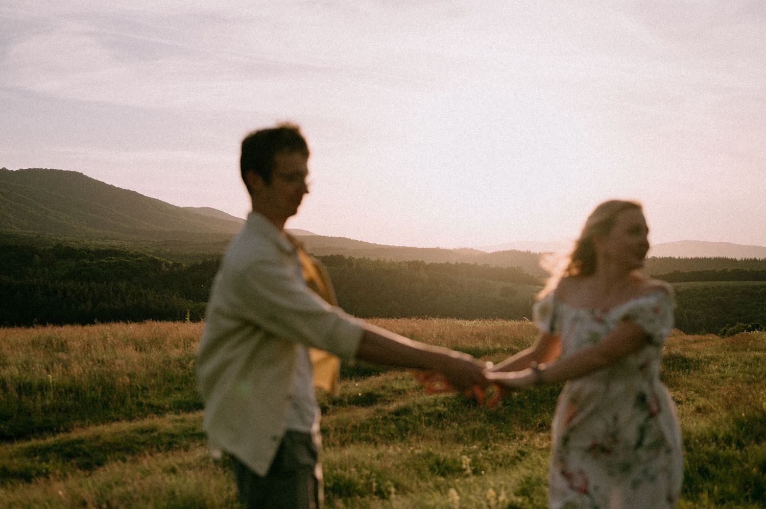 Couple dancing and spinning together in mountain field at golden hour.