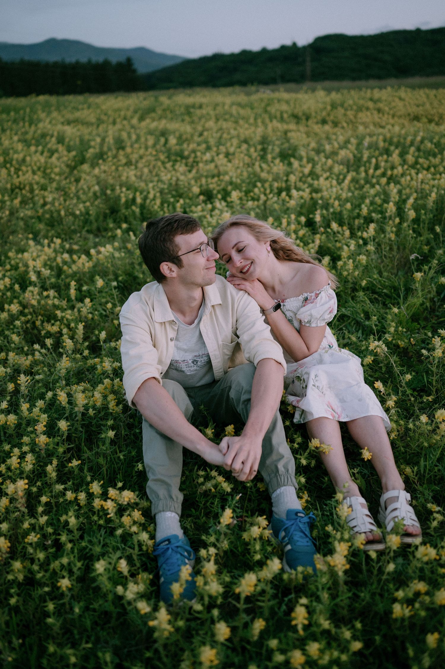 Two people share a tender moment while sitting in a blooming yellow flower field.