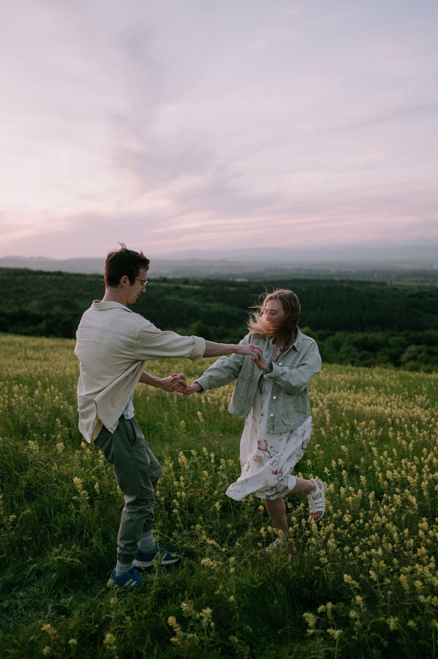 Two people dance and spin together in a meadow filled with yellow flowers at twilight.
