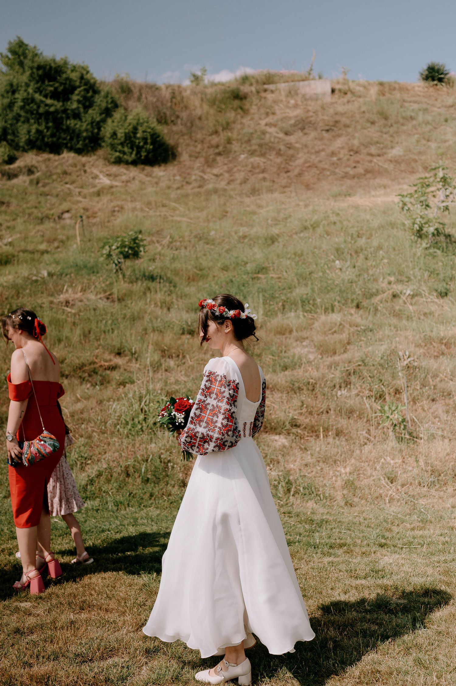 Wedding attendants in coral dresses and white dresses walking across a grassy hillside.