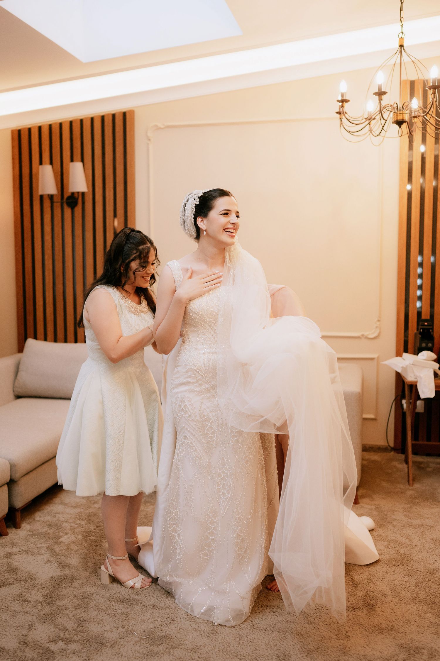 Candid wedding preparation shots showing laughter and joy while arranging the bridal attire.