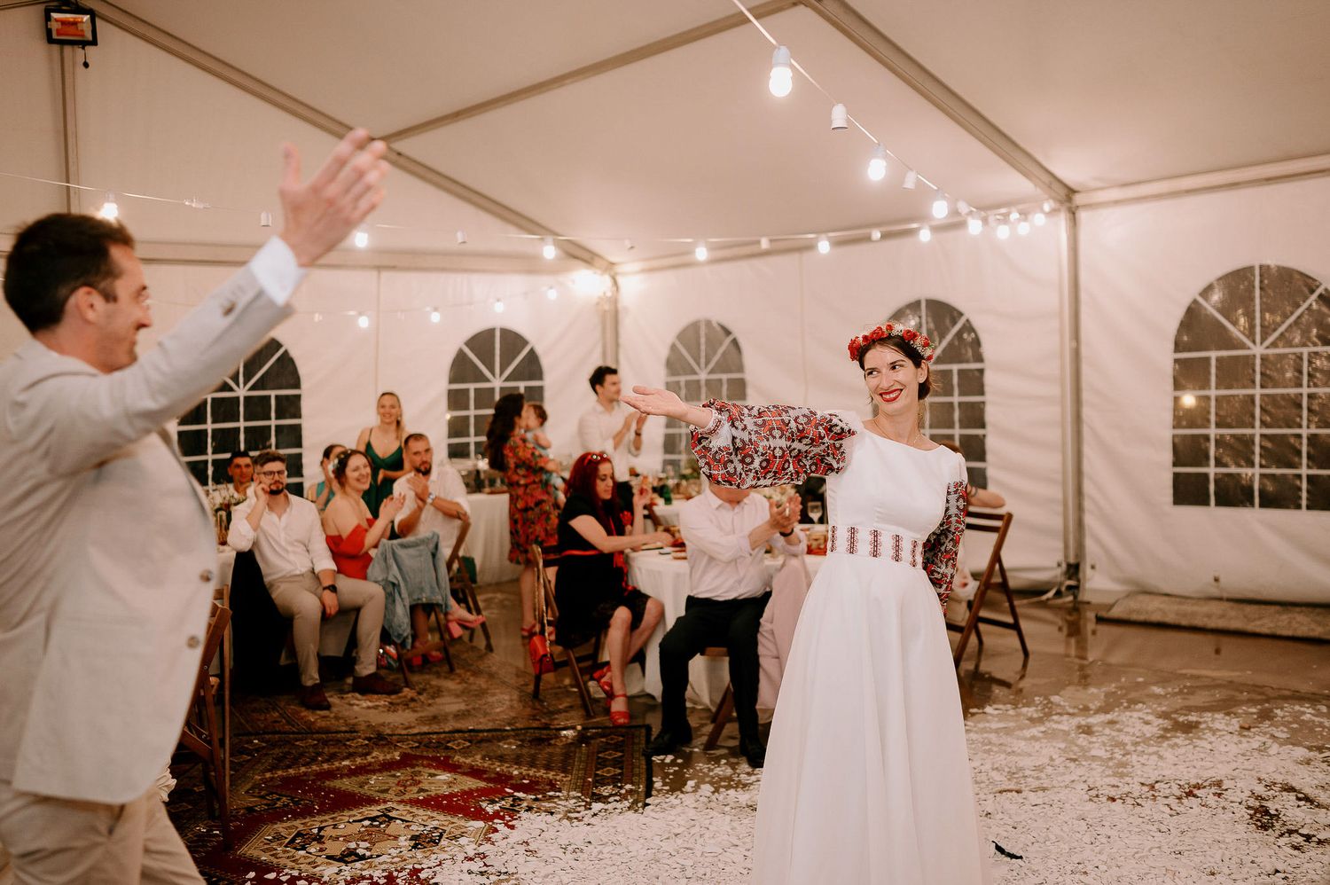 Wedding celebration in a white tent with guests dancing amidst scattered confetti.