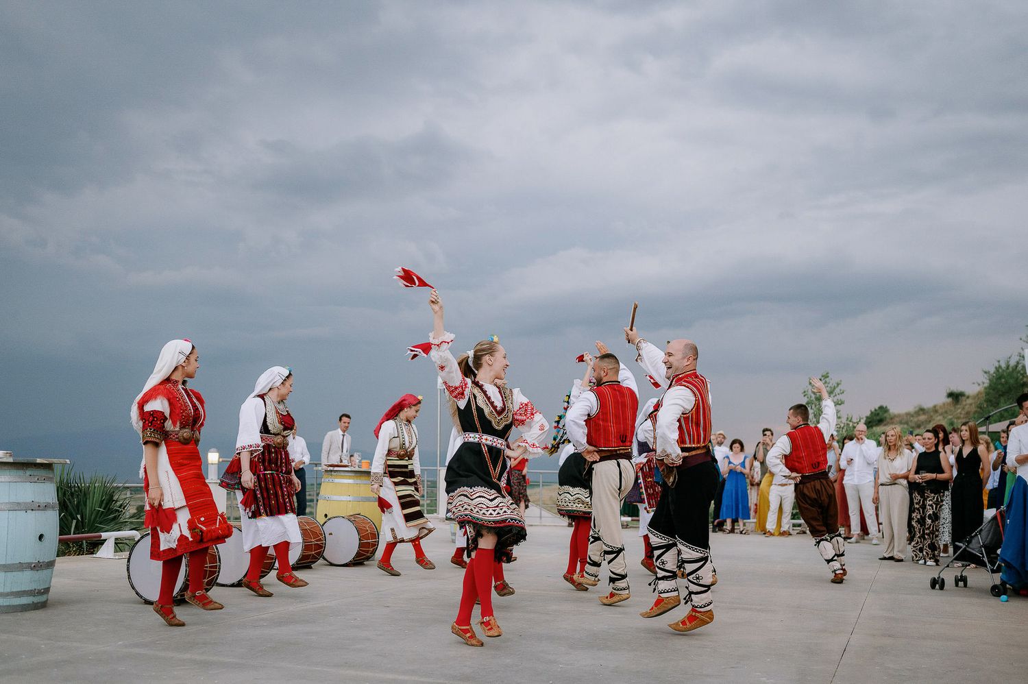 A group of folk dancers in red and white costumes perform at an outdoor festival.