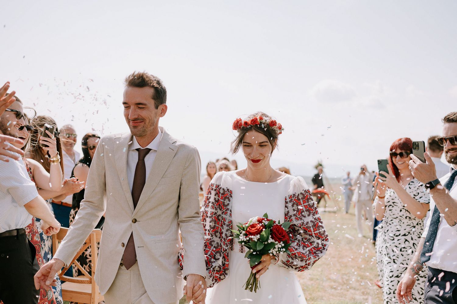 A couple walks hand in hand during their wedding recessional as guests toss confetti in celebration.