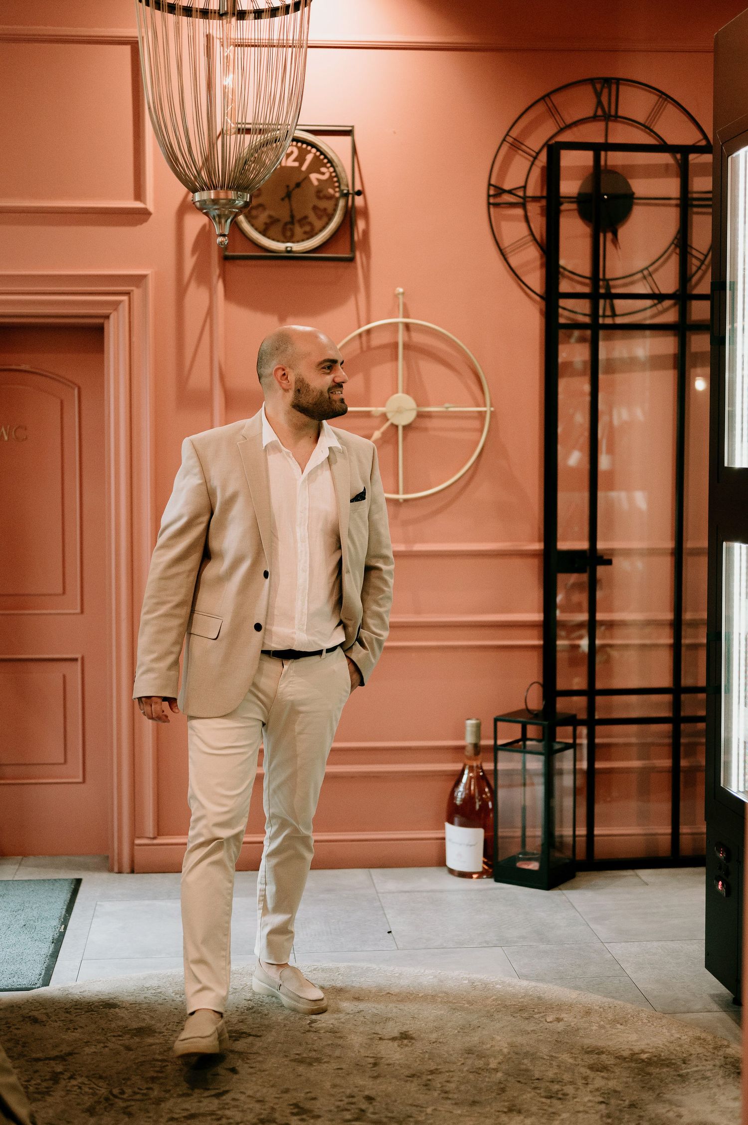 A figure in light colored attire stands in an elegant room with salmon-pink walls and vintage decor.