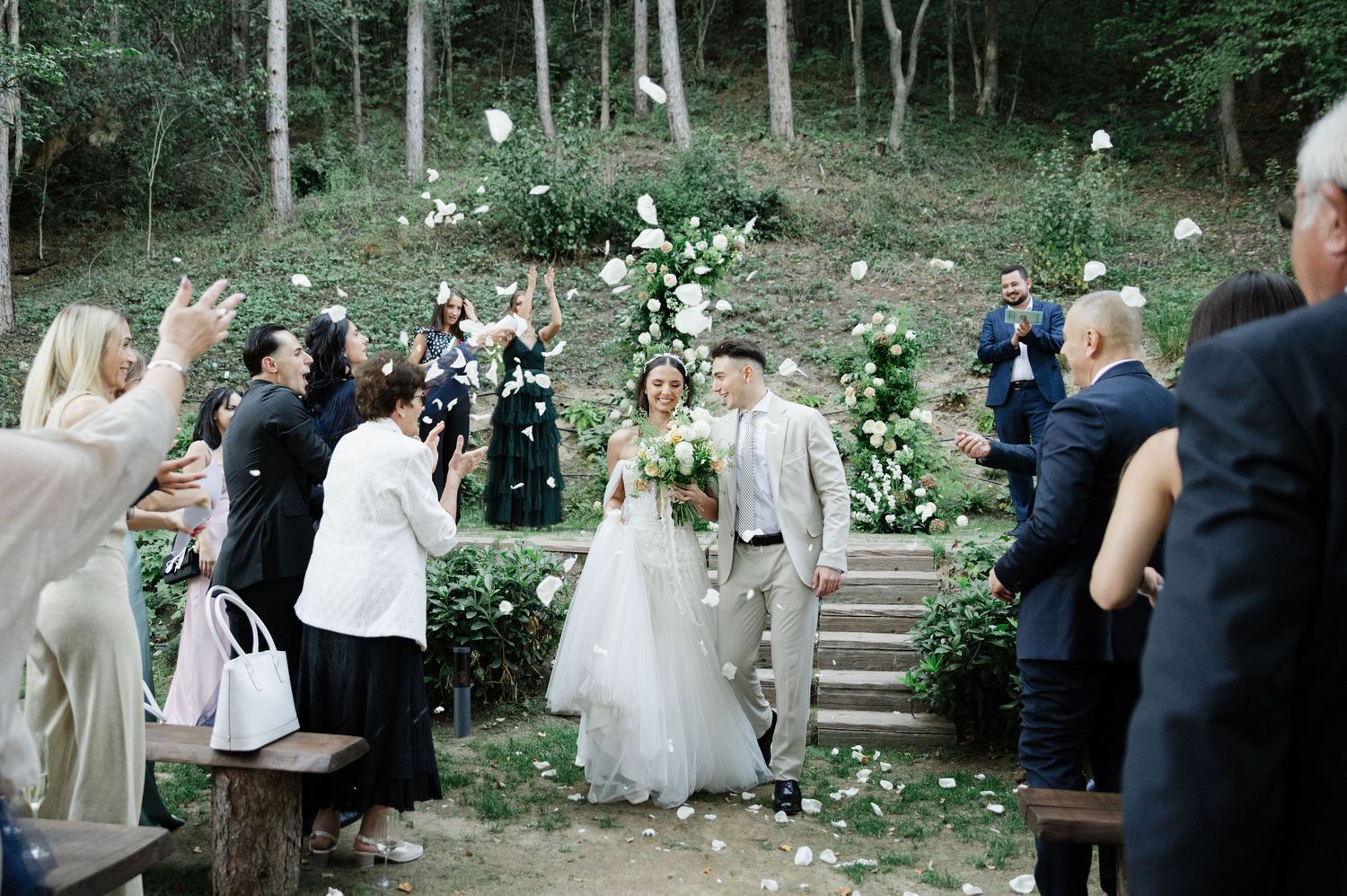 Wedding guests celebrating in an outdoor forest amphitheater with stone steps.