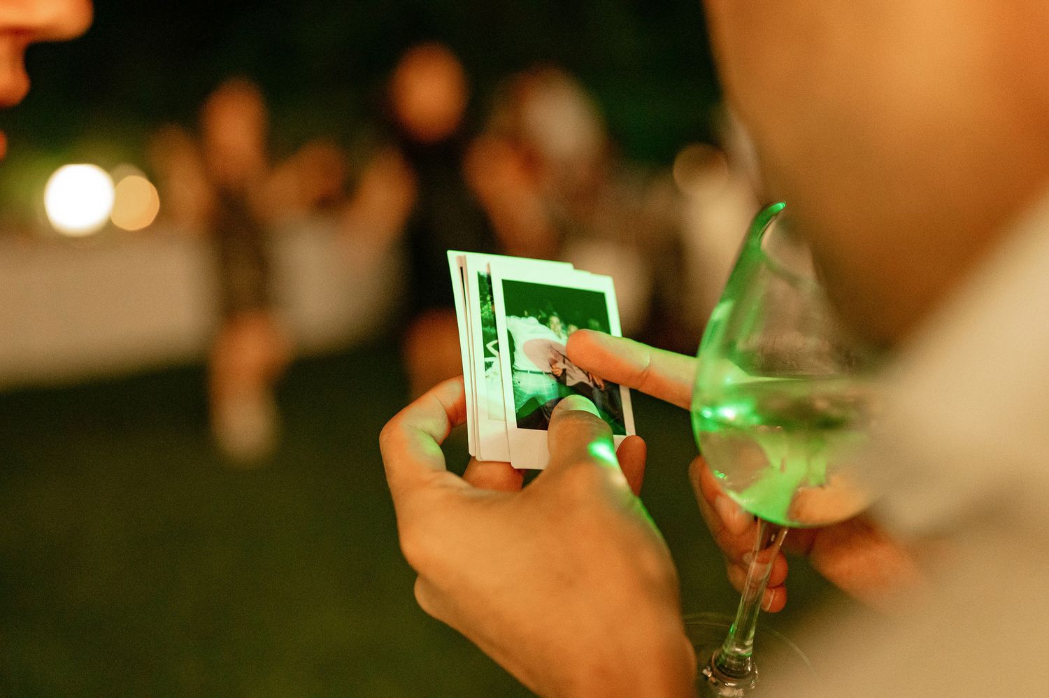 Close-up of hands holding and examining a polaroid photo at night.