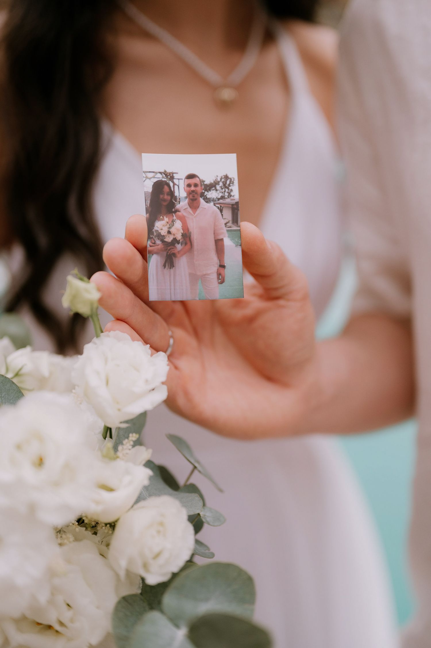 Hands holding a small photograph with white flowers in the foreground.