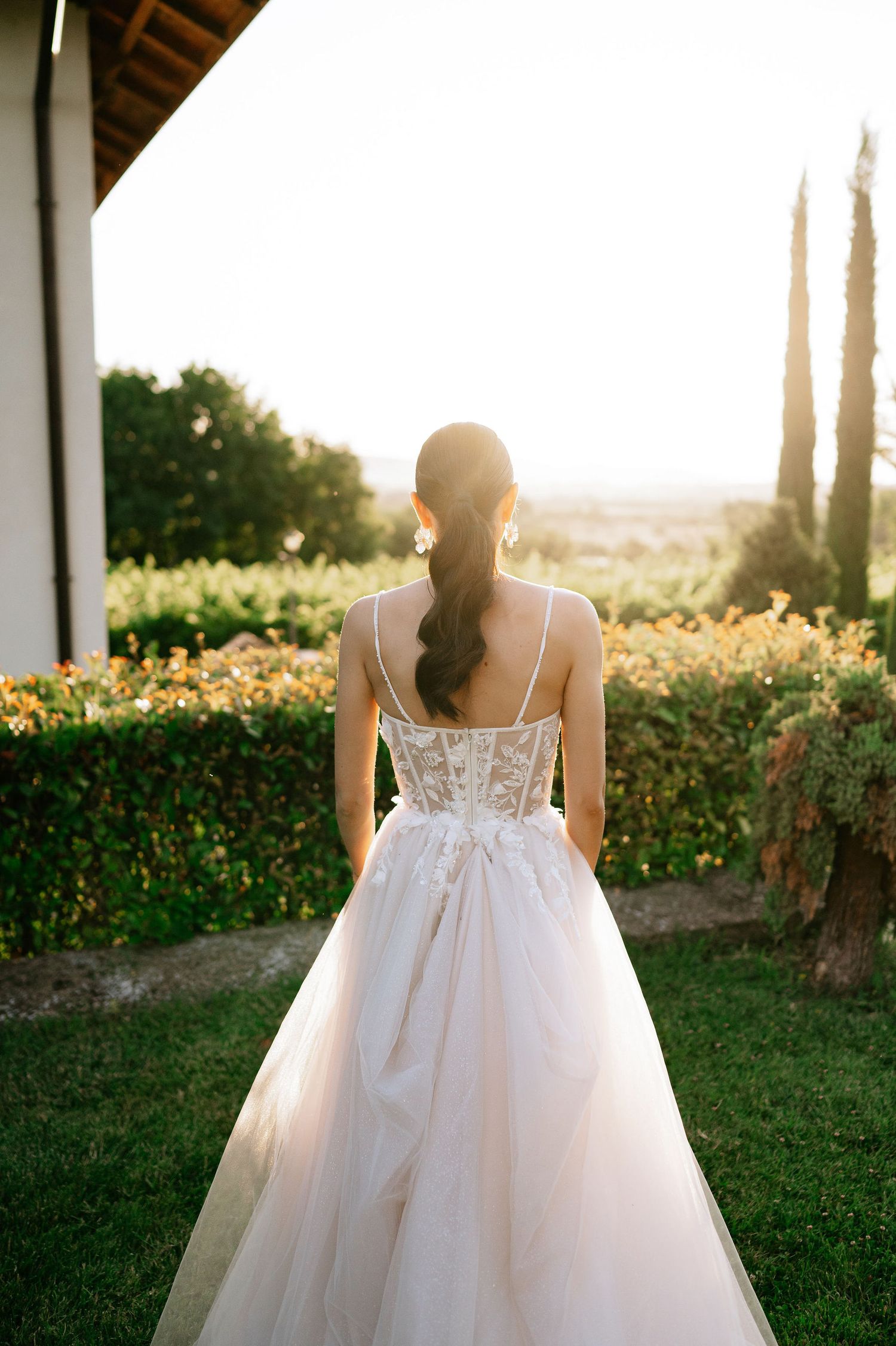 Back detail of a wedding gown with sheer lace bodice in garden setting at sunset.