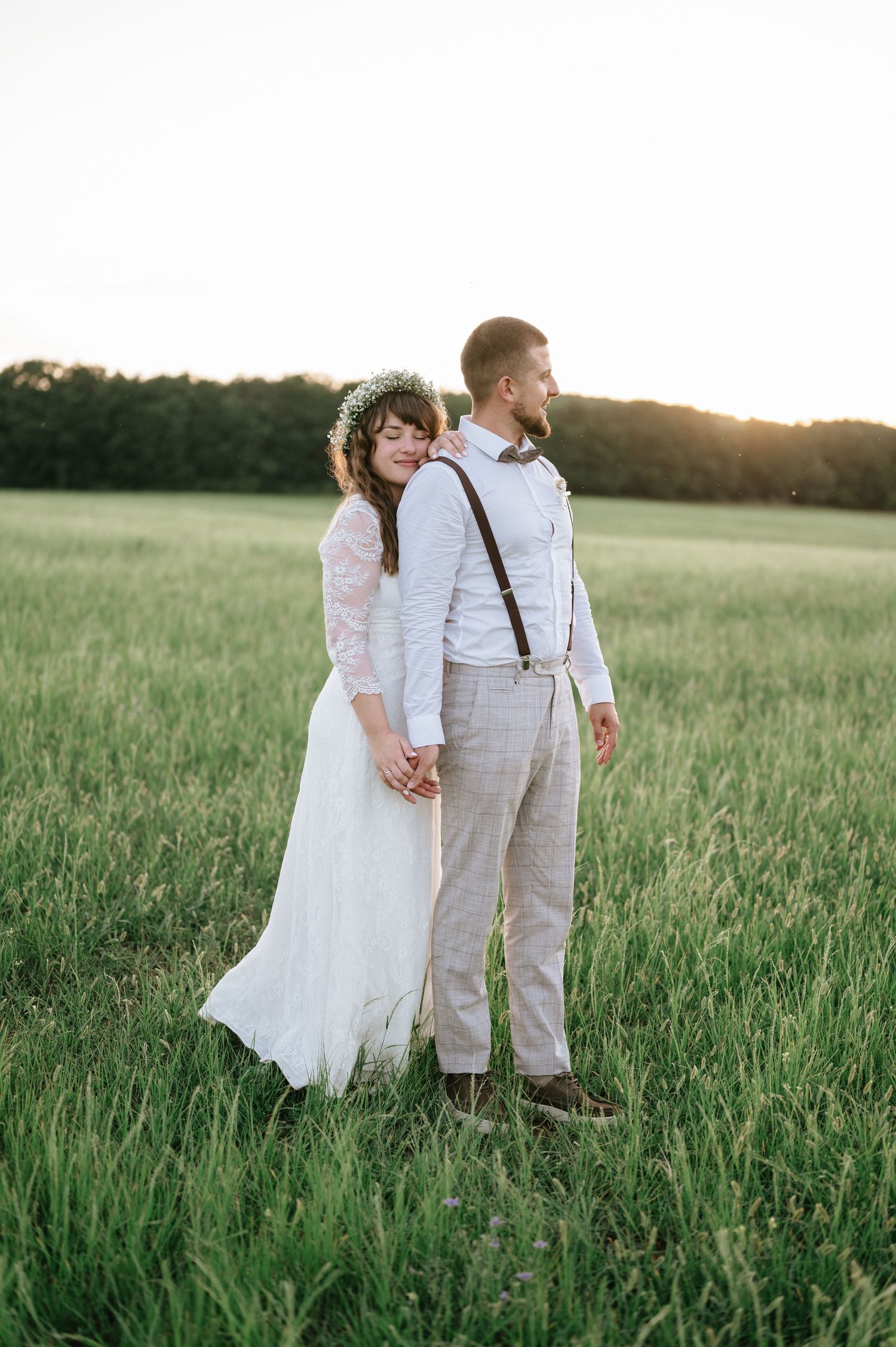 A couple stands together in tall grass during their countryside wedding photoshoot.
