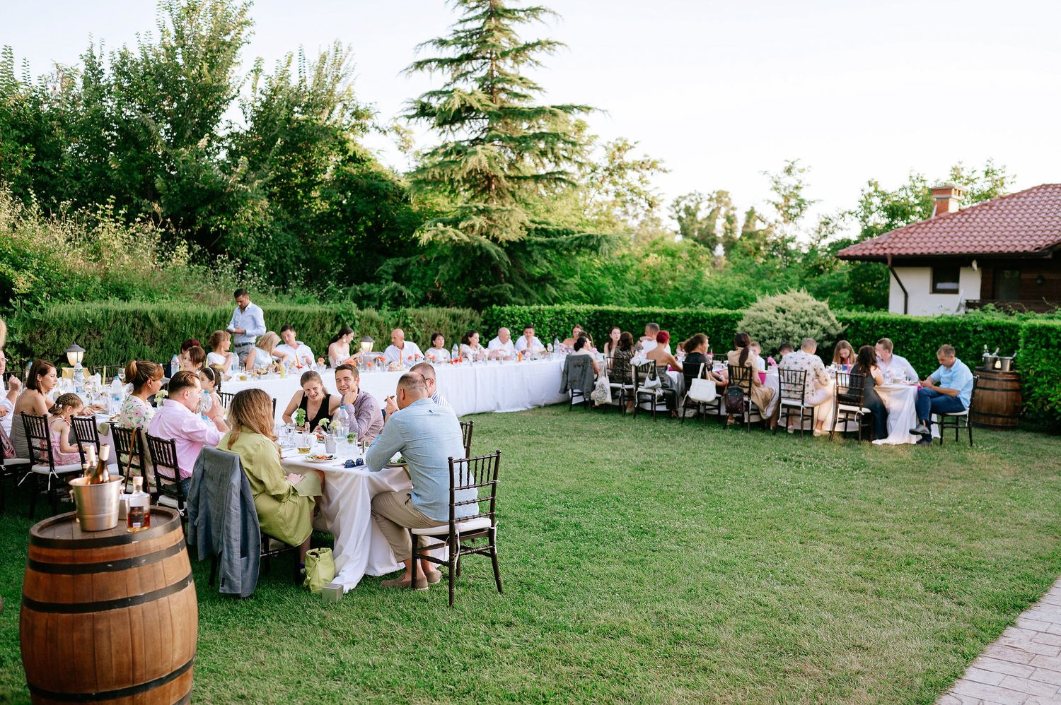Outdoor wedding reception setup with white tables and chairs on a grassy lawn at sunset.