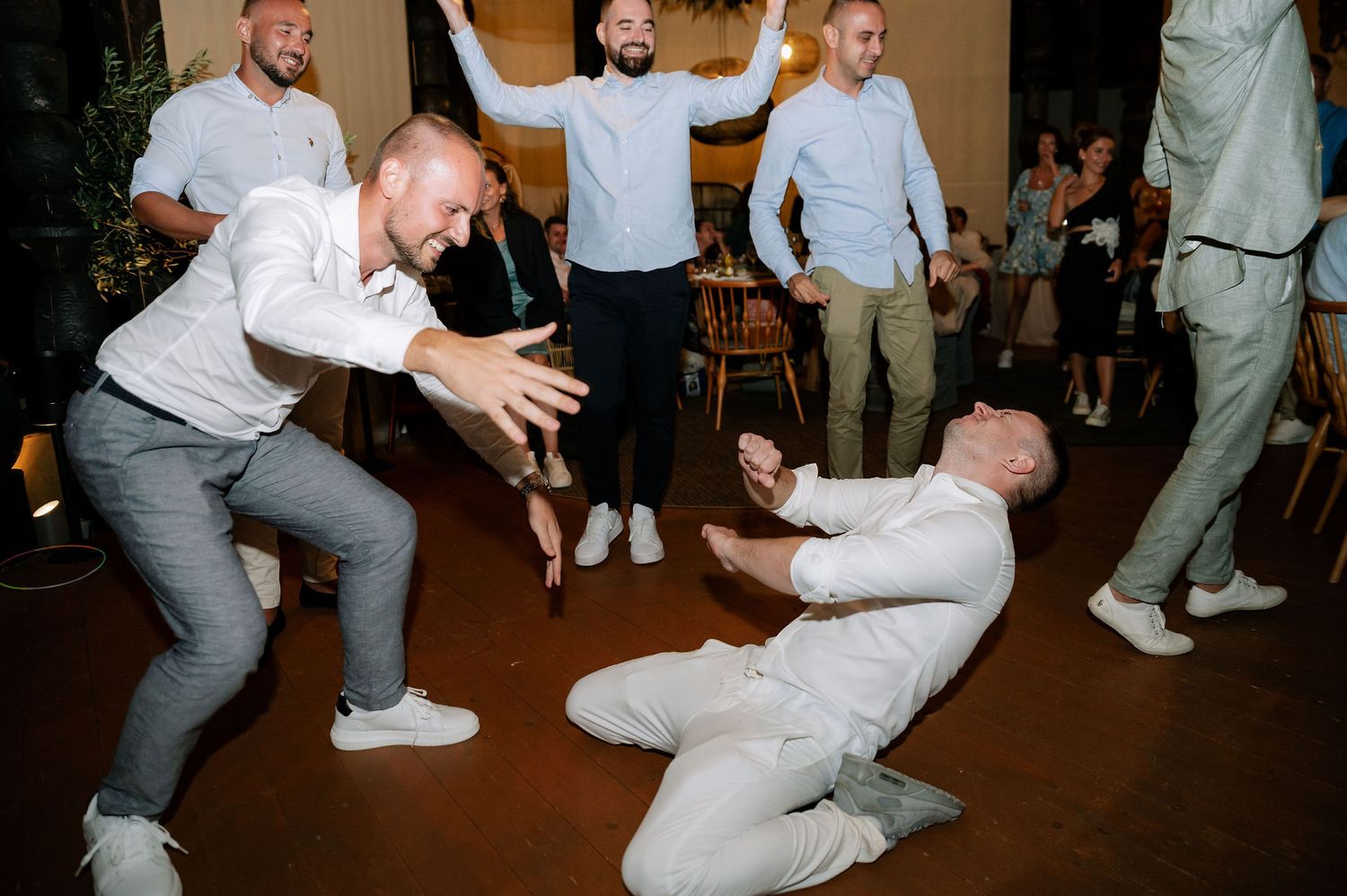 Wedding guests performing energetic dance moves on a reception dance floor.