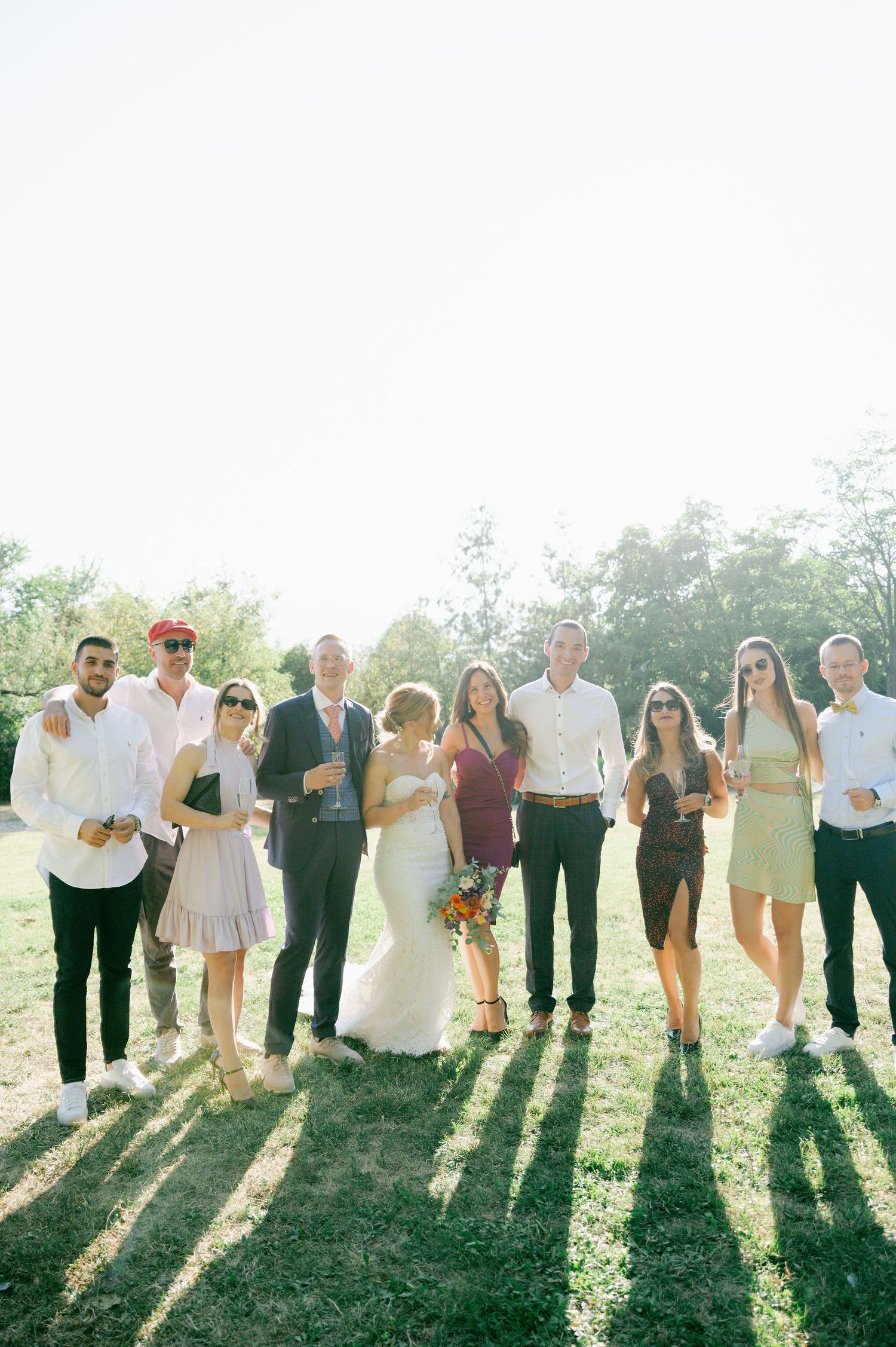 Wedding party poses together casting long shadows on green grass during golden hour.