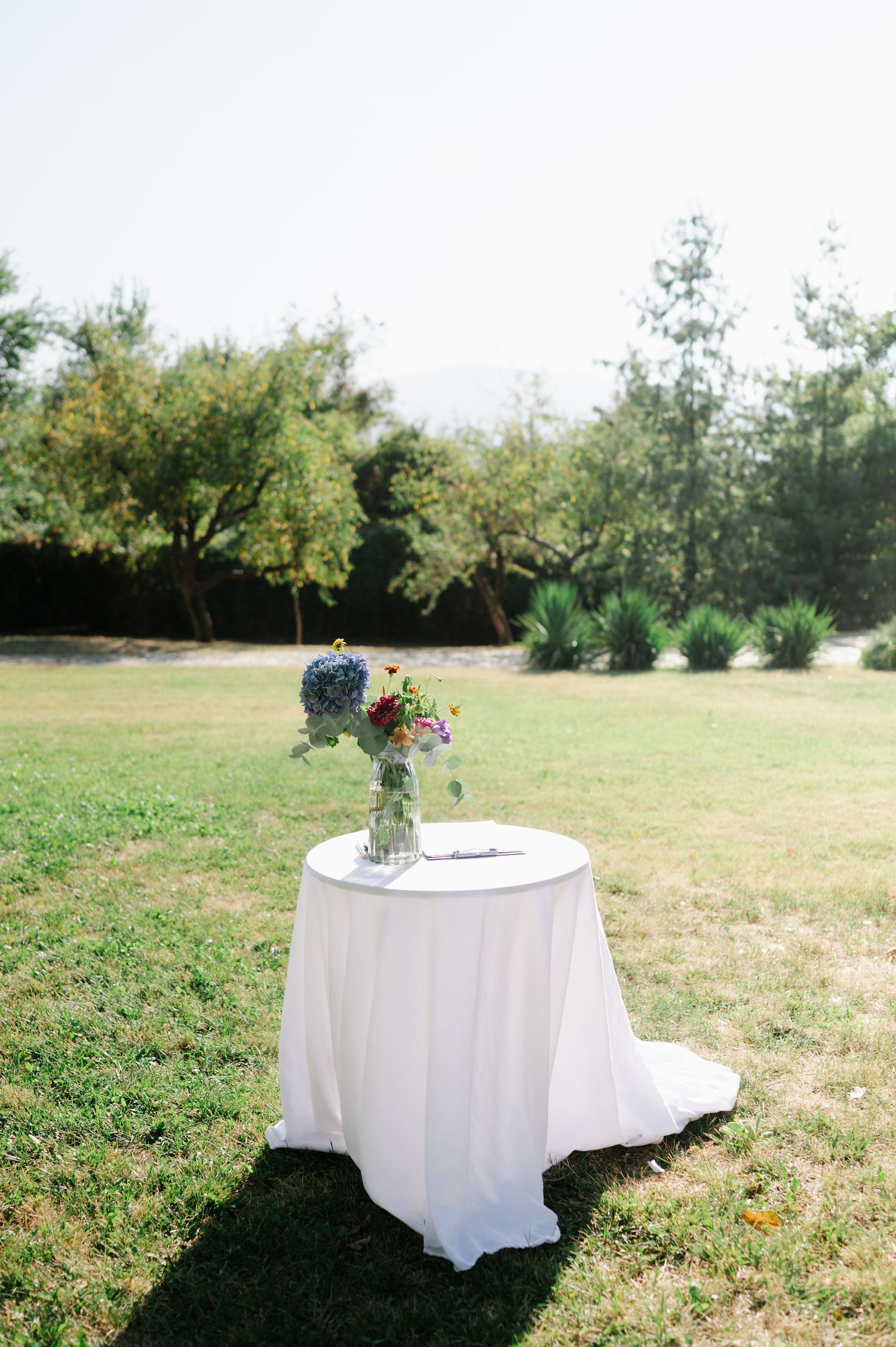 White round tables with floral centerpieces set up in an outdoor field.