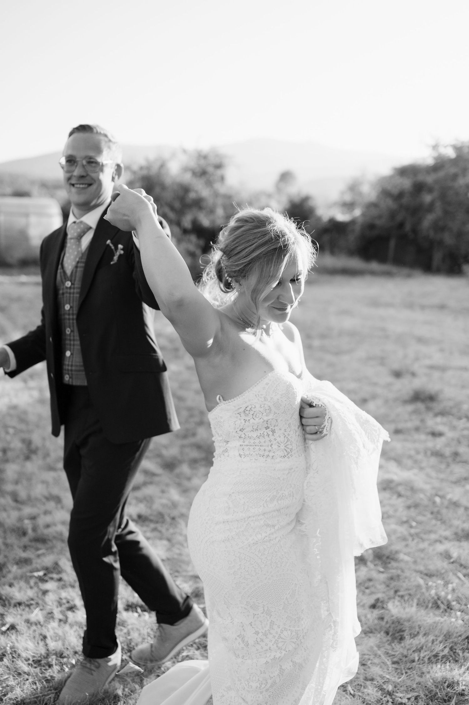 Dancing newlyweds twirl through a sun-drenched field during their wedding photoshoot.