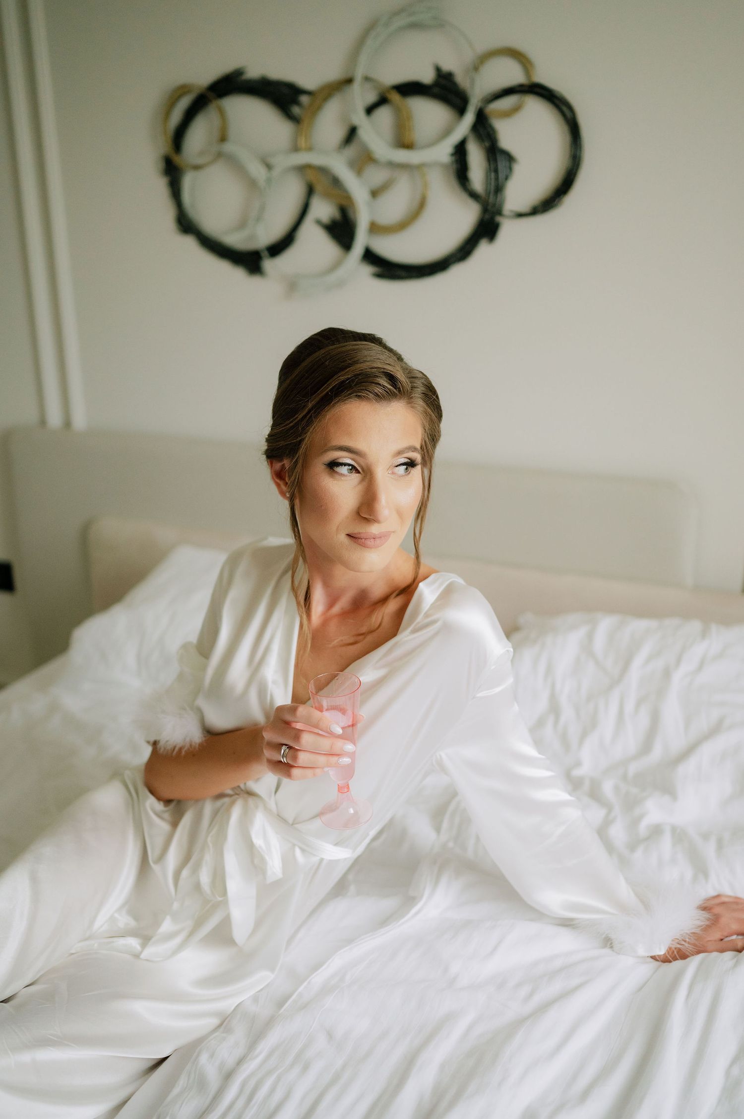Woman in white robe enjoying a celebratory drink while lounging on bed.