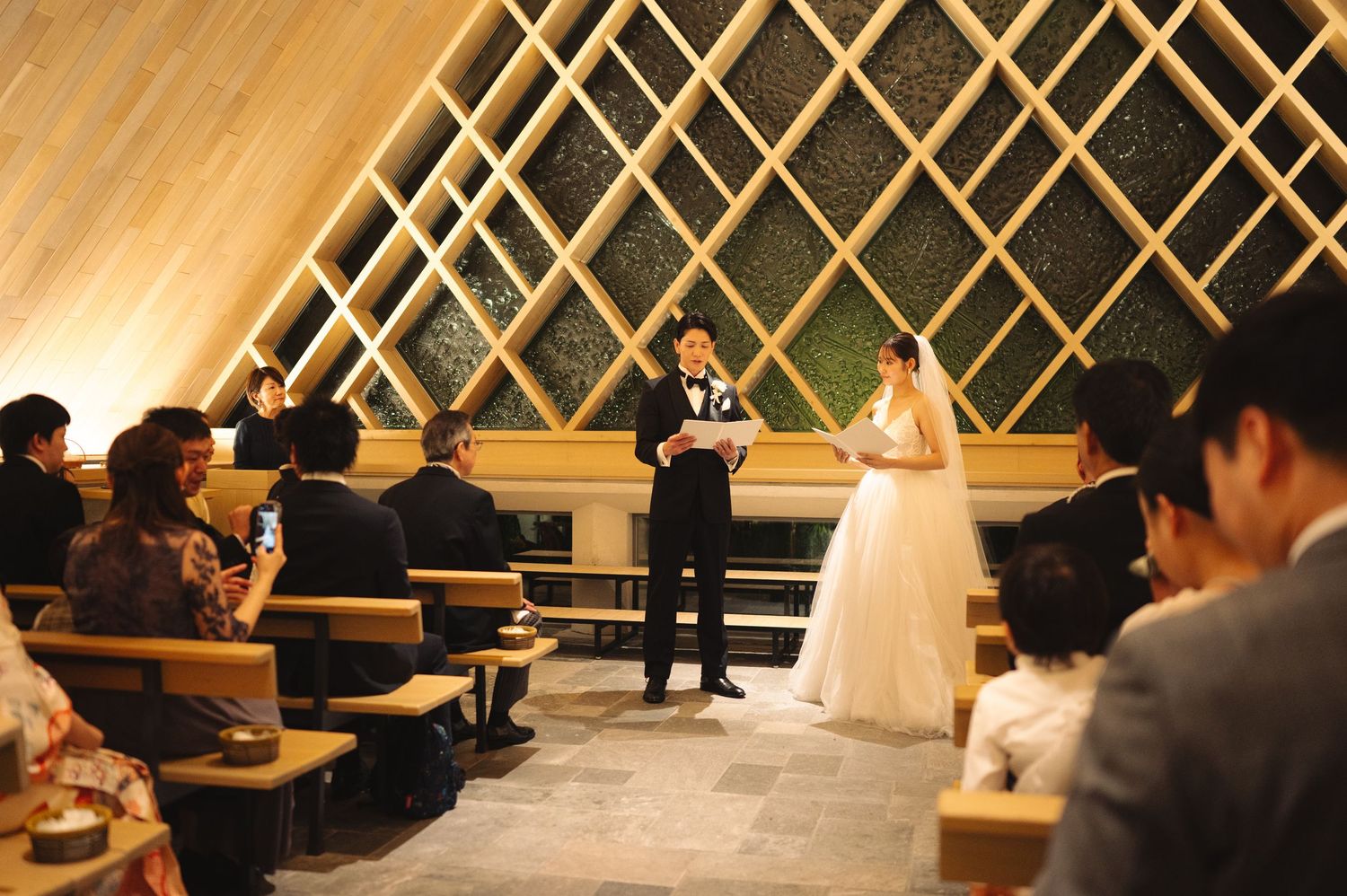 Wedding ceremony in progress inside a modern chapel with striking lattice wall architecture.