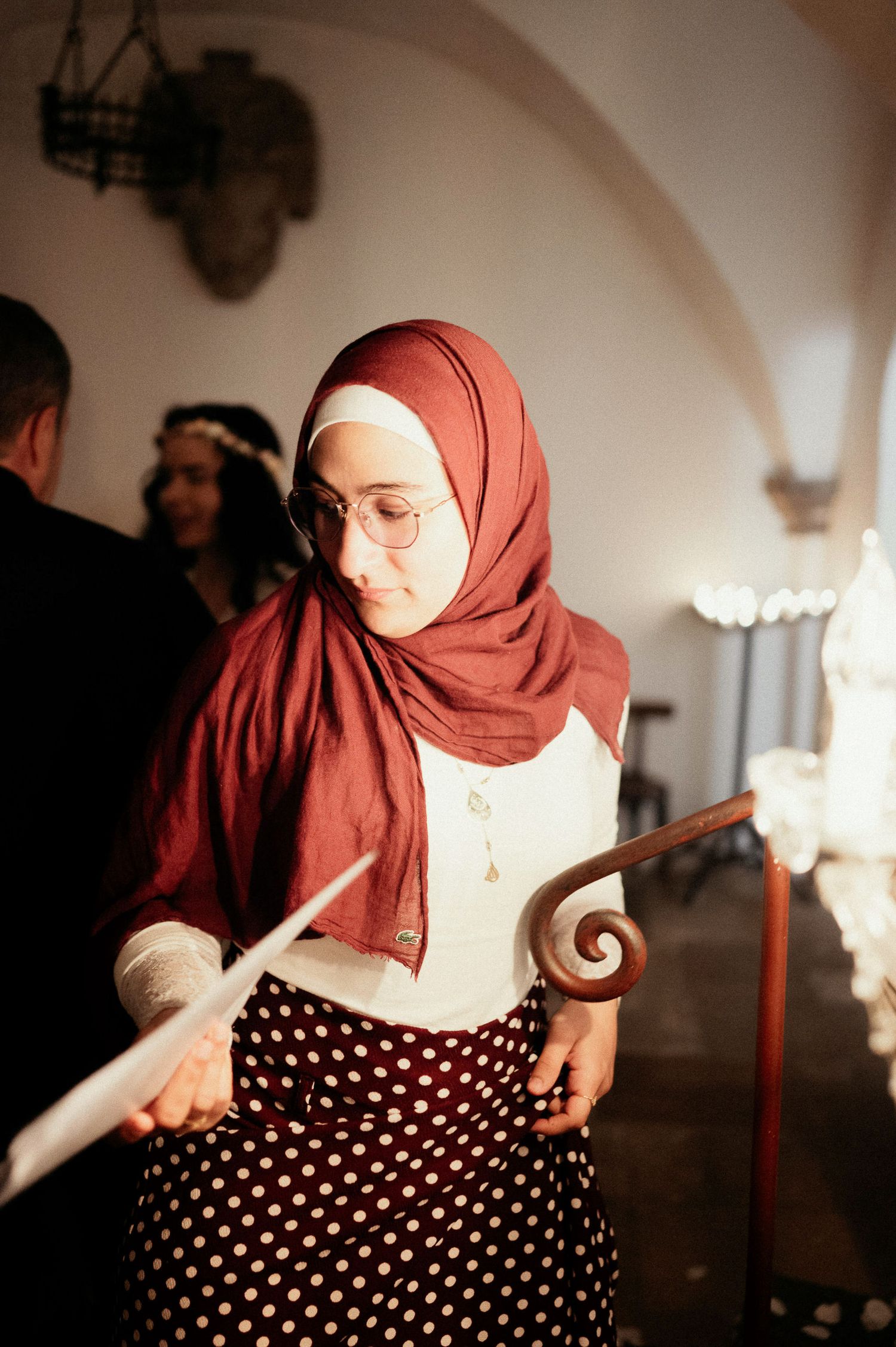Person in polka dot dress and burgundy hijab poses playfully in an arched hallway.
