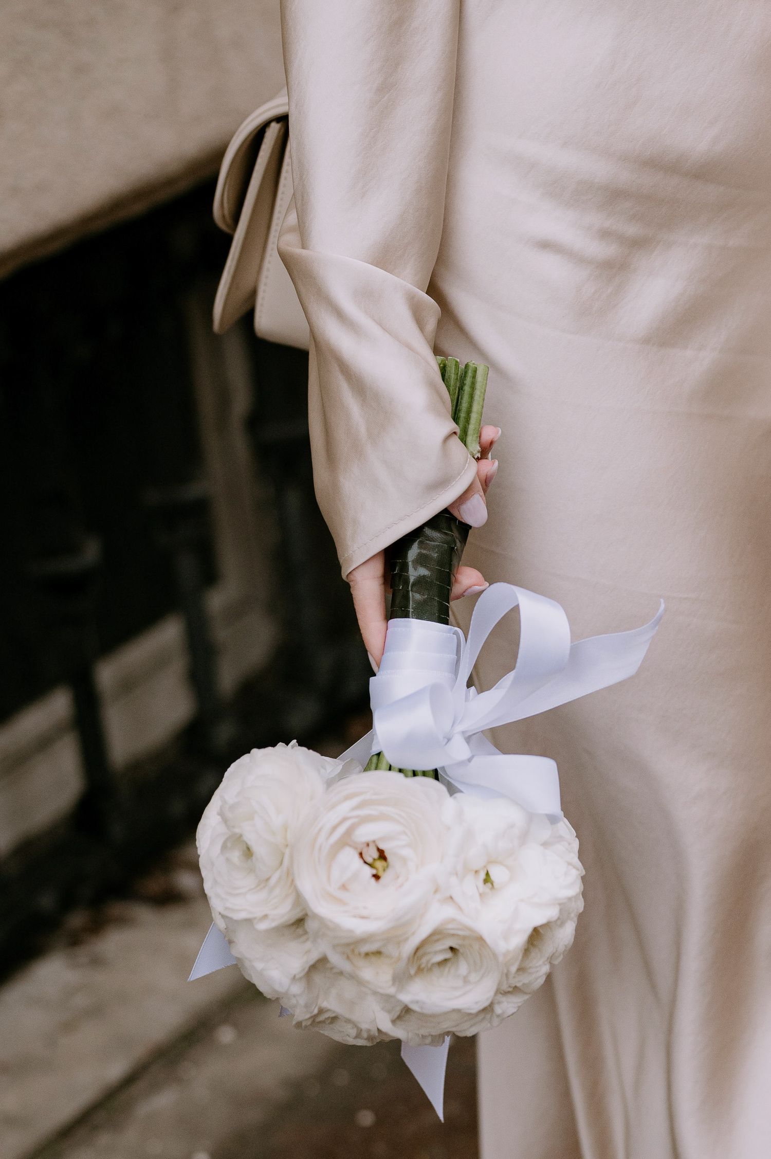 A white bridal bouquet of fresh roses being held against a light-colored dress.