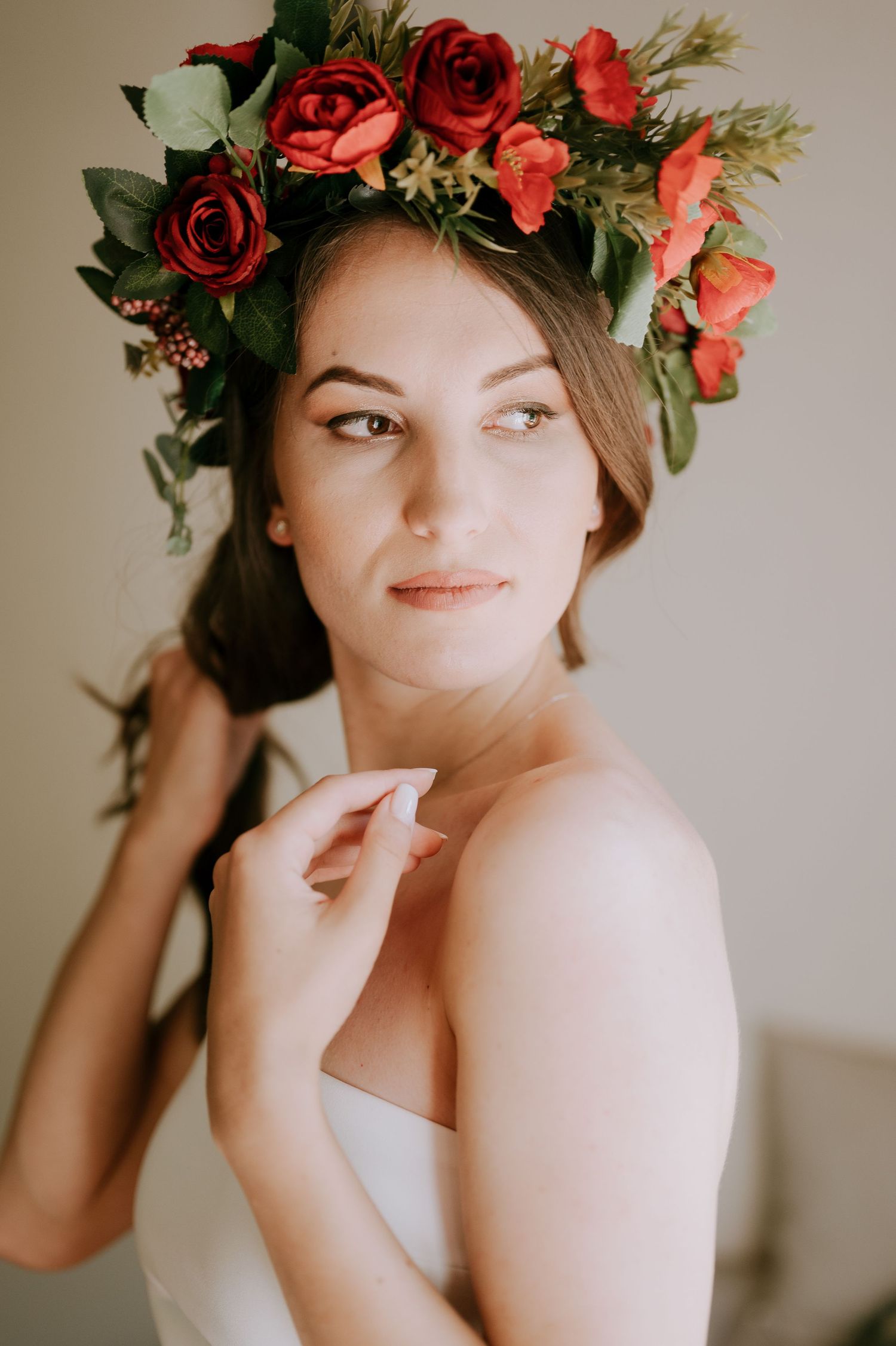 Close-up portrait wearing a red rose flower crown and white dress in dreamy window light.