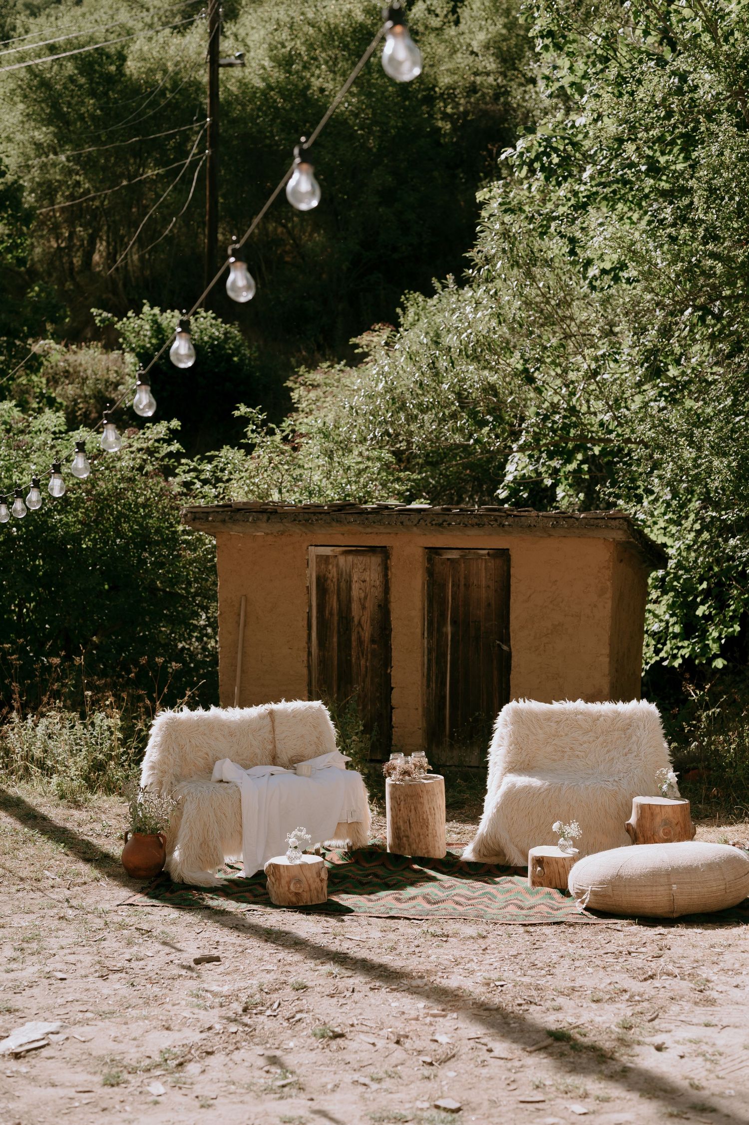 White outdoor seating arrangements set up in a garden setting with string lights.