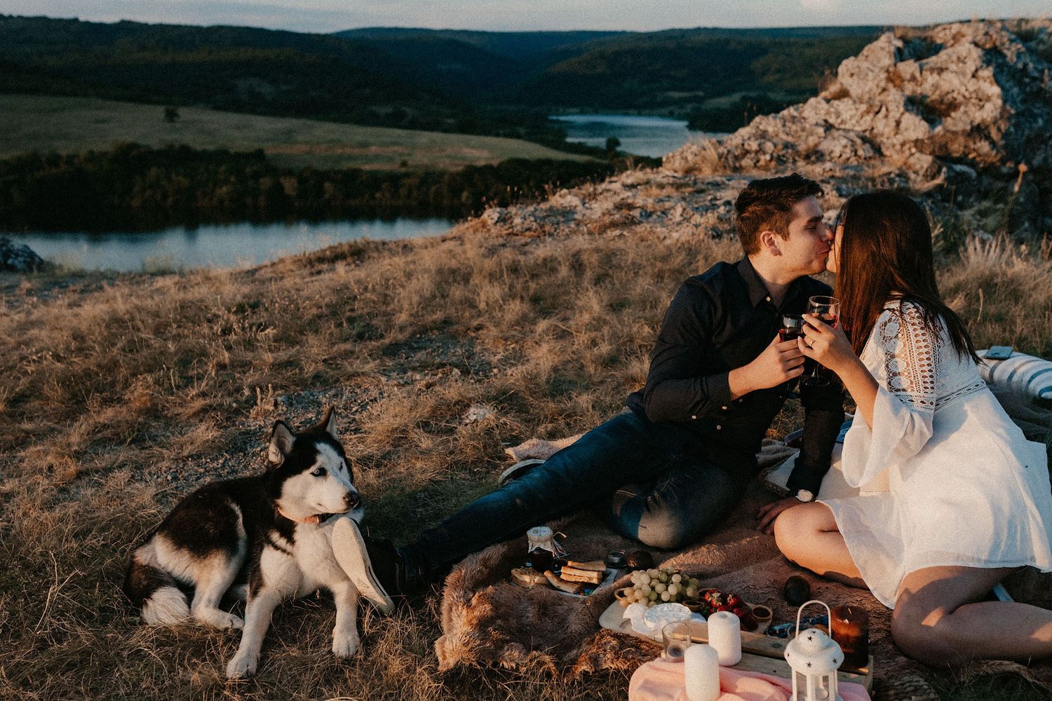 A romantic picnic scene set against a scenic hillside landscape at golden hour.