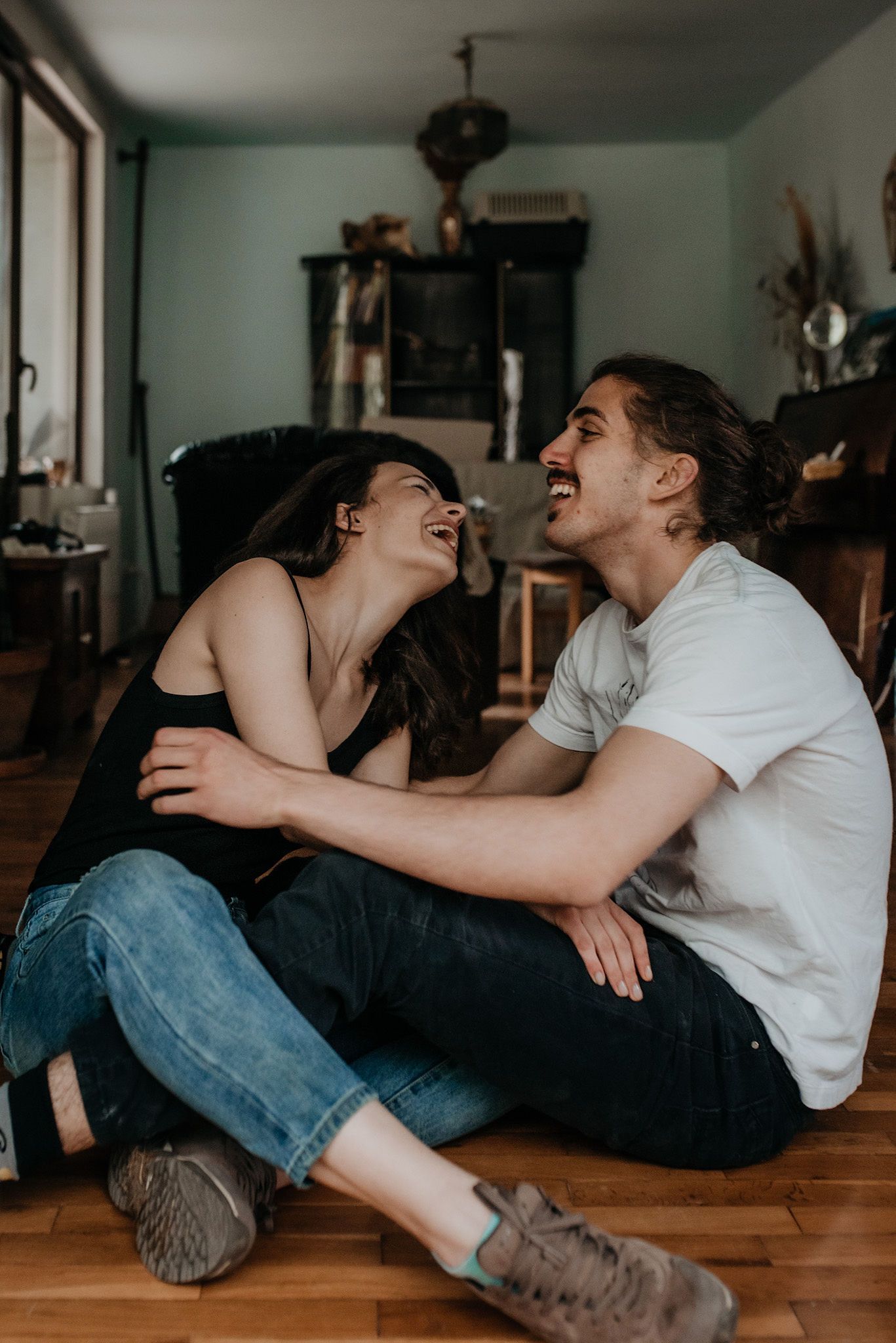 A couple sitting on wooden floor laughing together in a cozy living room setting.