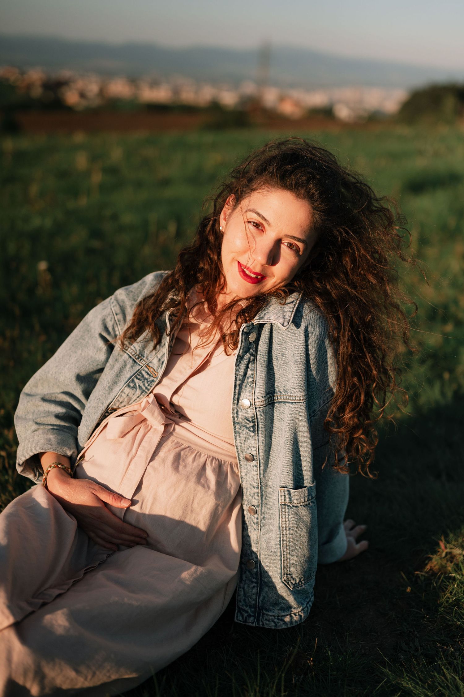 A person in a denim jacket poses expressively in a grassy field during golden hour sunset lighting.