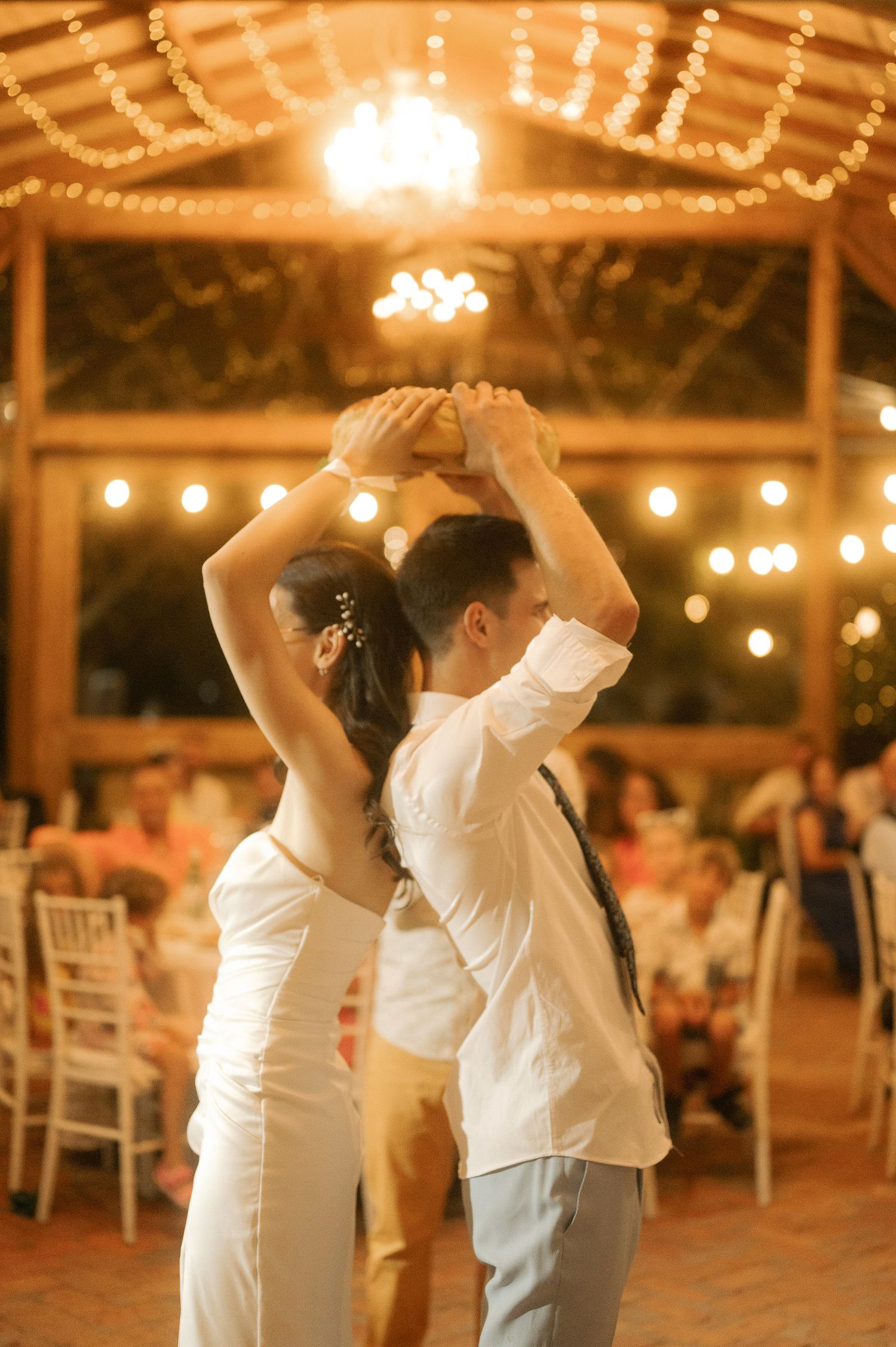 A couple dances together at a wedding reception under warm string lights in an elegant covered outdoor venue.