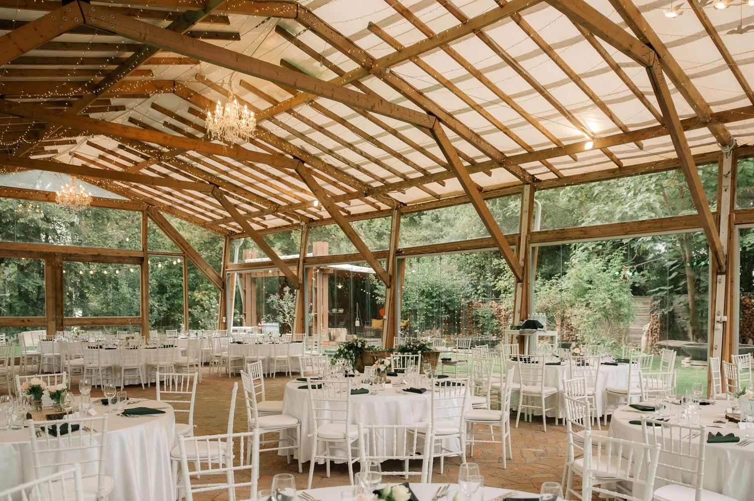 Rustic wooden pavilion set up for a wedding reception with white tables and chairs under exposed beam ceiling.