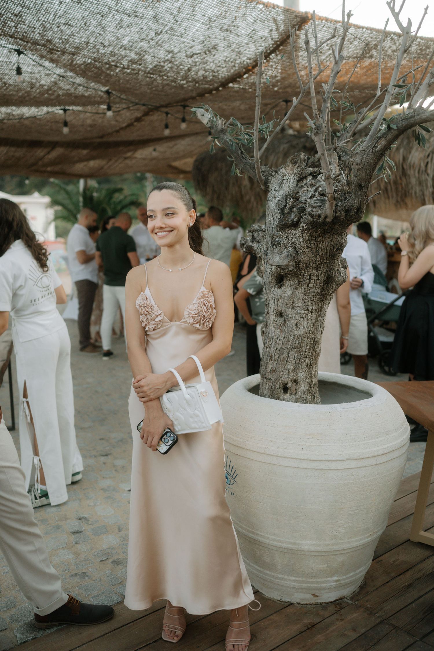 Outdoor event under rustic canopy with large decorative pottery and guests mingling in casual elegant attire.