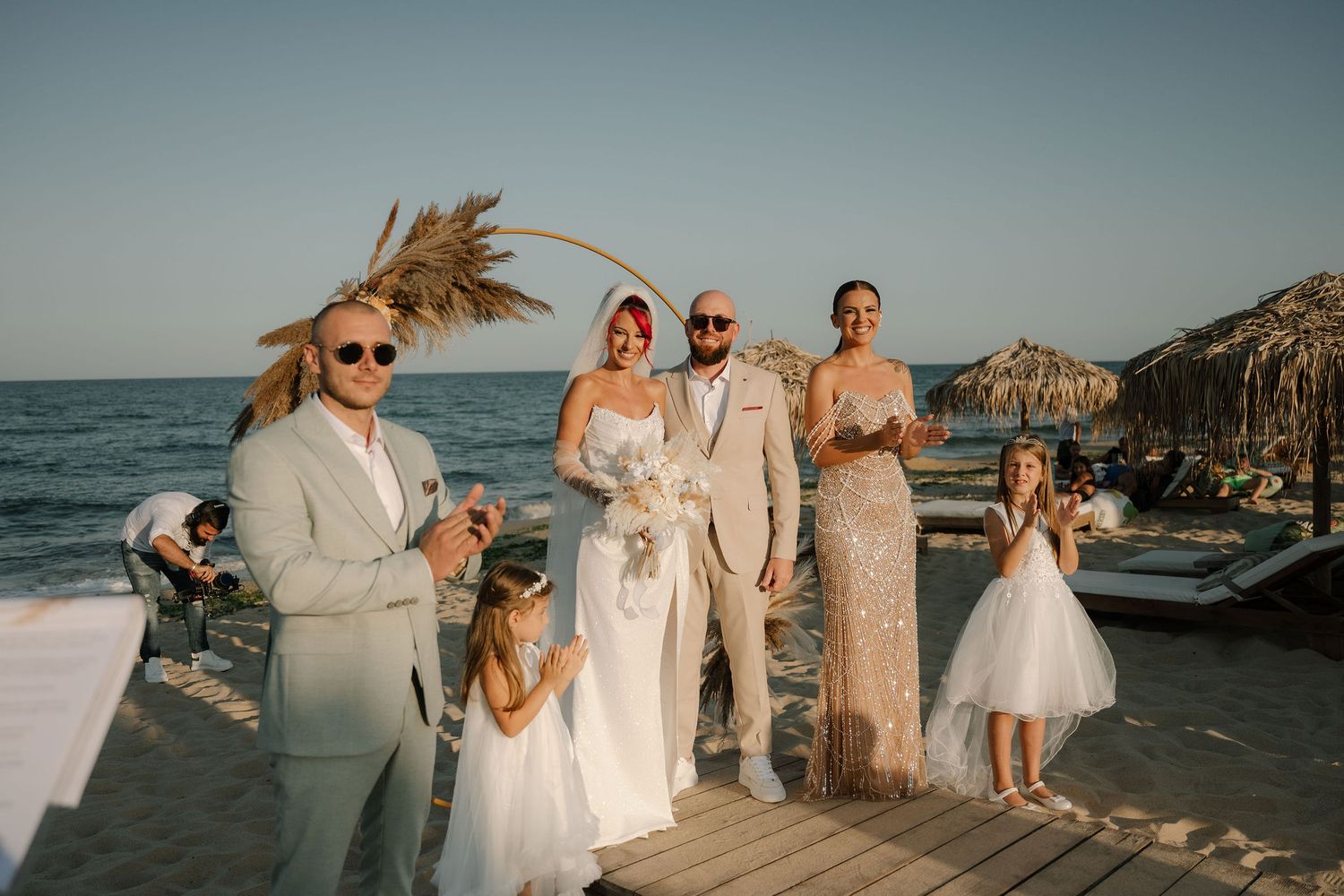 A wedding party poses together on a beach boardwalk with ocean and cliffs in the background during sunset.