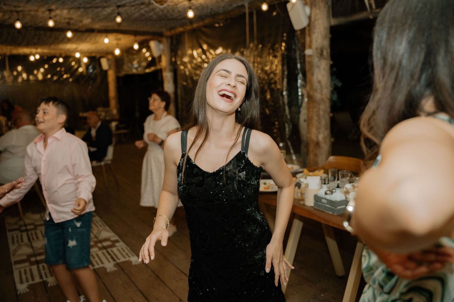People dancing and celebrating at a dimly lit wedding reception with string lights overhead.