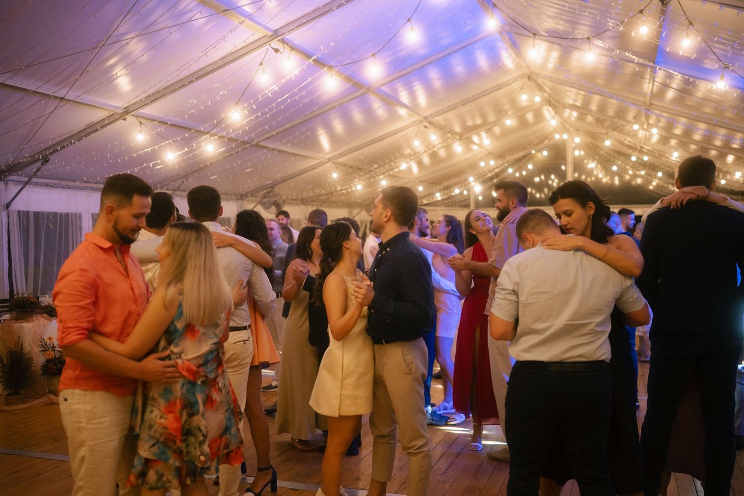 Wedding celebration in a tent venue with purple lighting and string lights creating a romantic atmosphere.