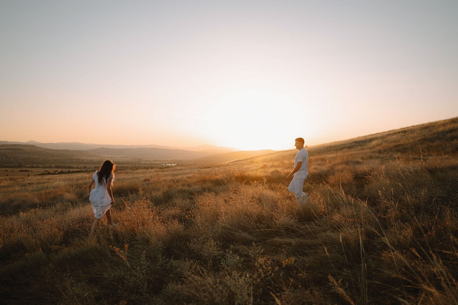 Panoramic view of silhouettes walking through golden grass fields at sunset with warm glowing sky.
