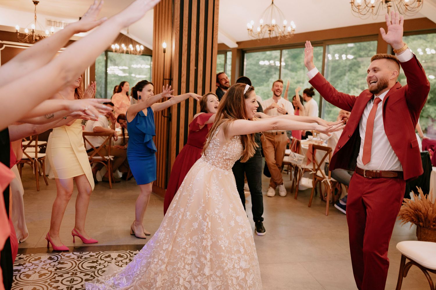Wedding guests dancing and celebrating on the dance floor at an elegant reception venue with chandeliers and wood accents.