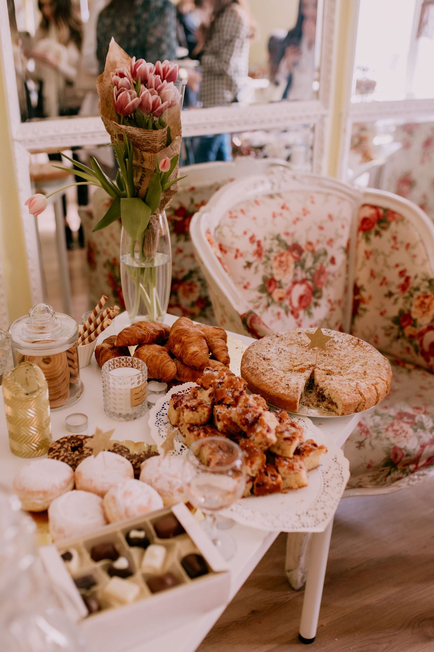 Elegant tea party setup with floral upholstered chairs, pastries, and desserts displayed on white cake stands.
