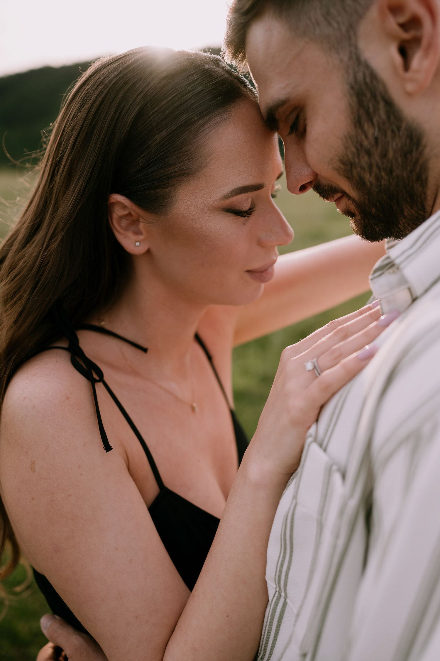 Intimate couple in romantic embrace outdoors with woman in black top and man in white shirt at sunset.