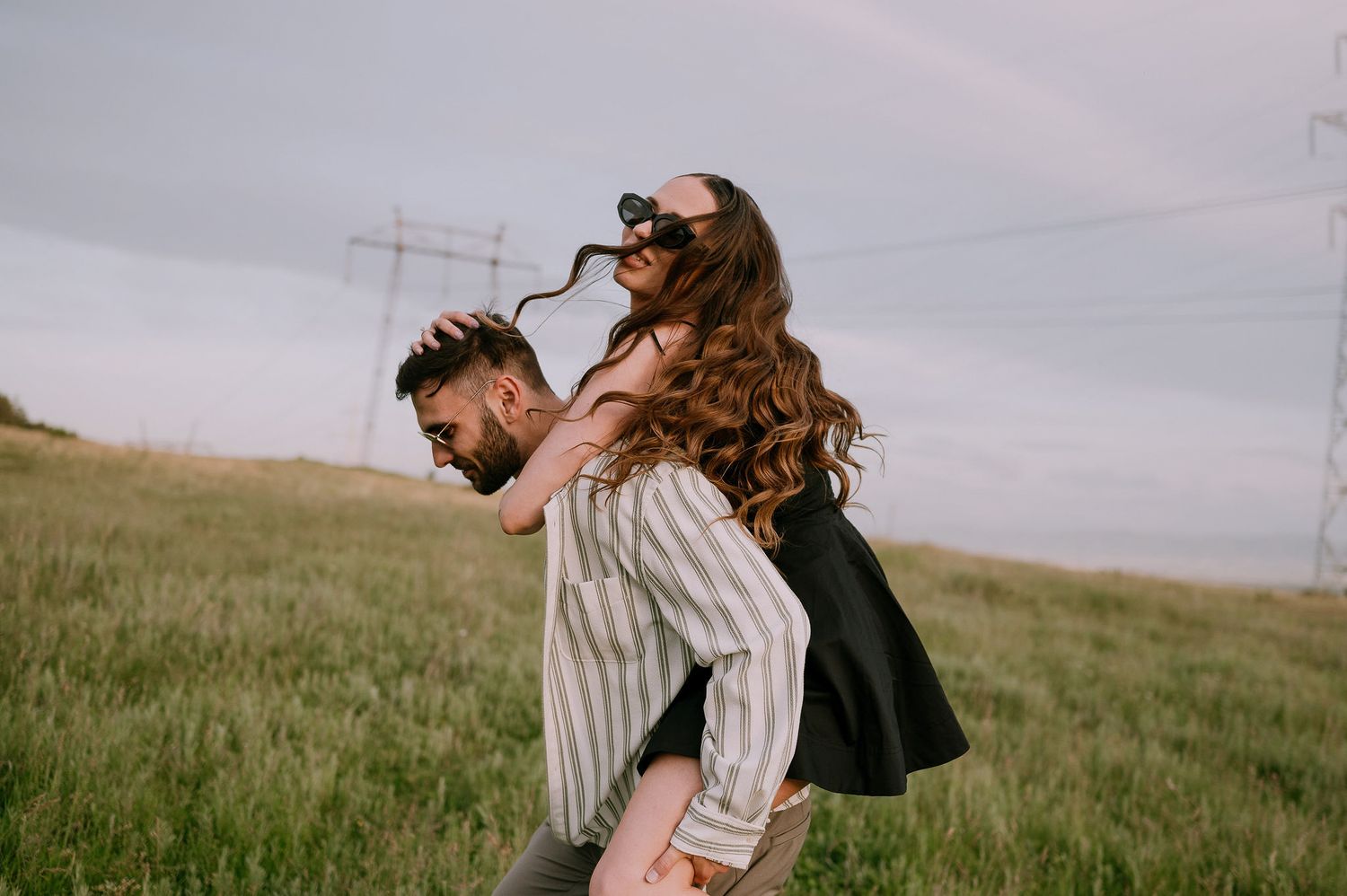 A couple shares a romantic moment together in a grassy meadow on a cloudy day.