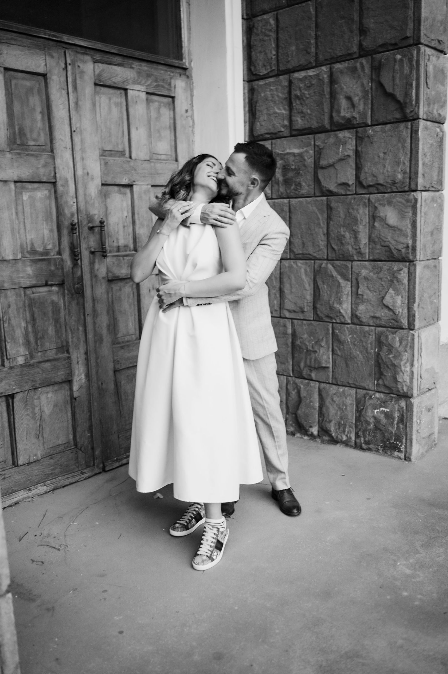 A black and white photo series showing three romantic moments between a couple in white clothing against a stone wall.