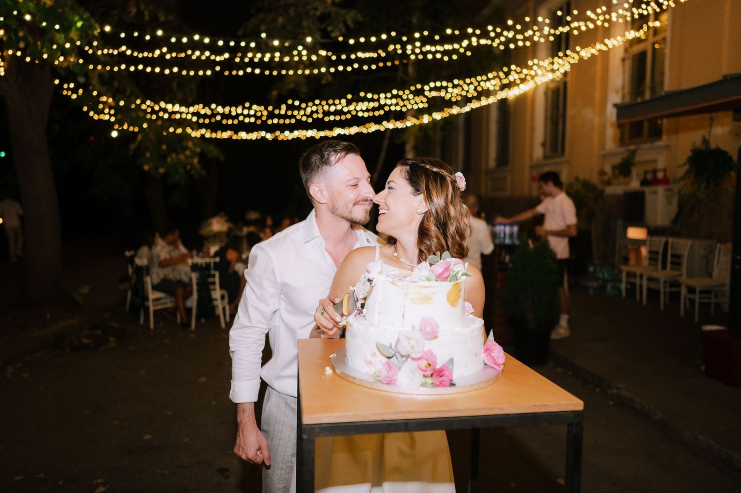 Romantic evening wedding reception outdoors with glowing string lights and couples dancing under the stars.