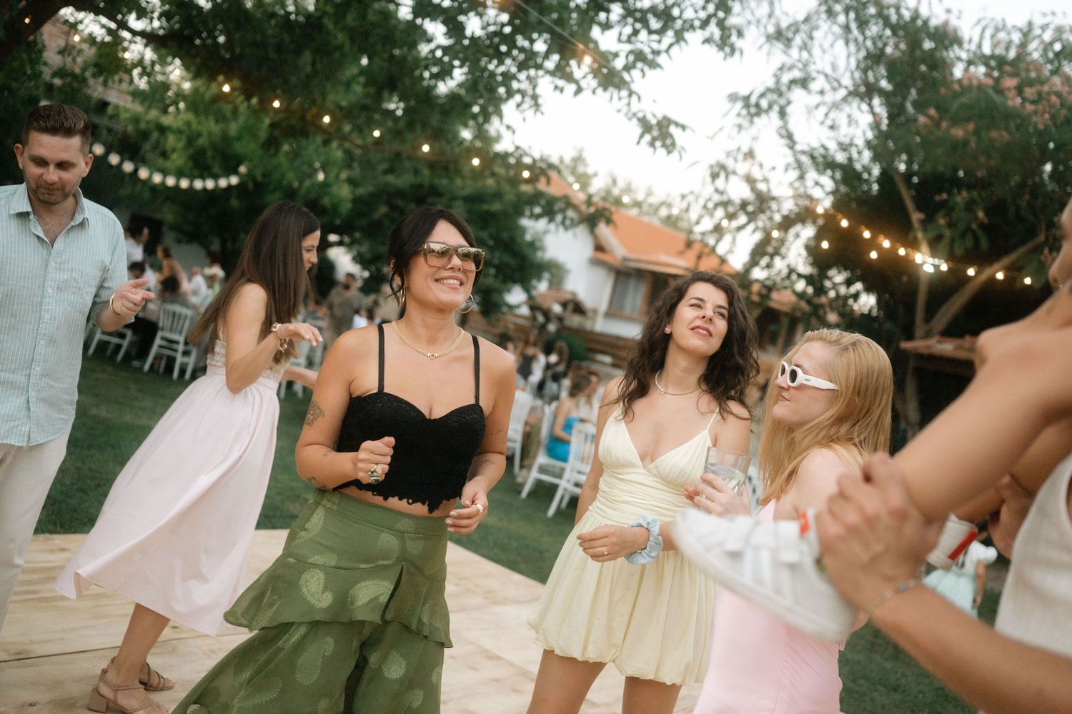 Wedding guests dancing and socializing under string lights at an outdoor evening celebration.
