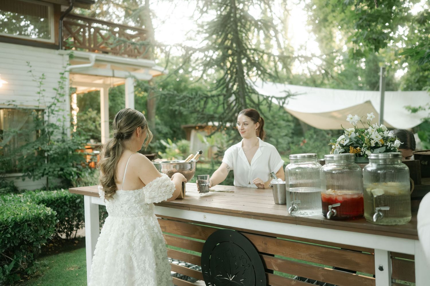 Elegant outdoor wedding reception setup with rustic wooden tables and white decor under string lights in a garden setting.