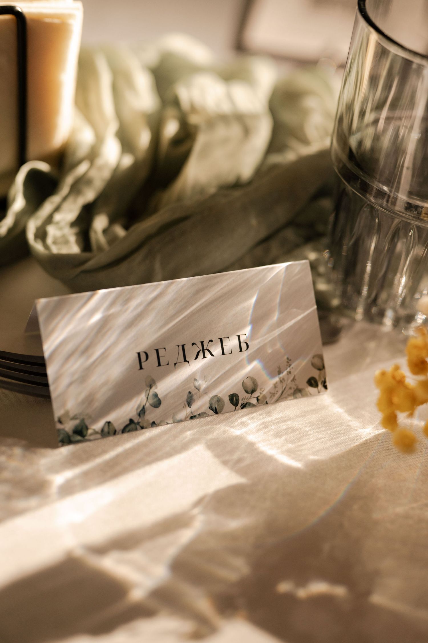 Close-up view of elegant place settings with name cards and glassware on white tablecloths in sepia tones.
