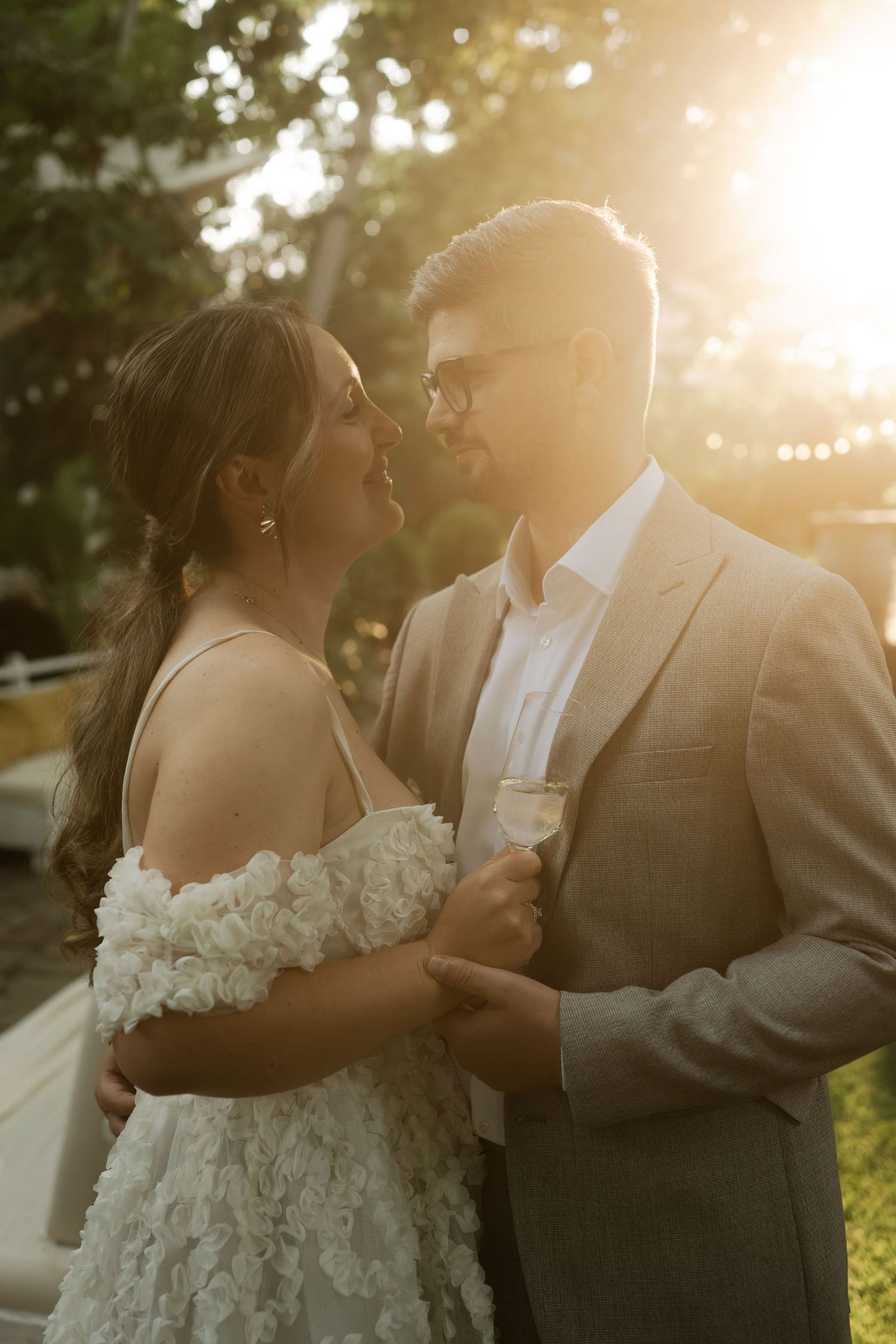 Romantic wedding couple embraces in golden sunlight during sunset photoshoot outdoors.