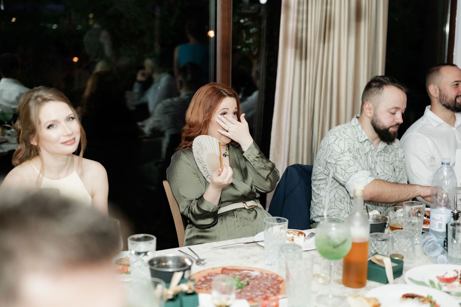 People gathered around tables at a social event or restaurant with drinks and food.