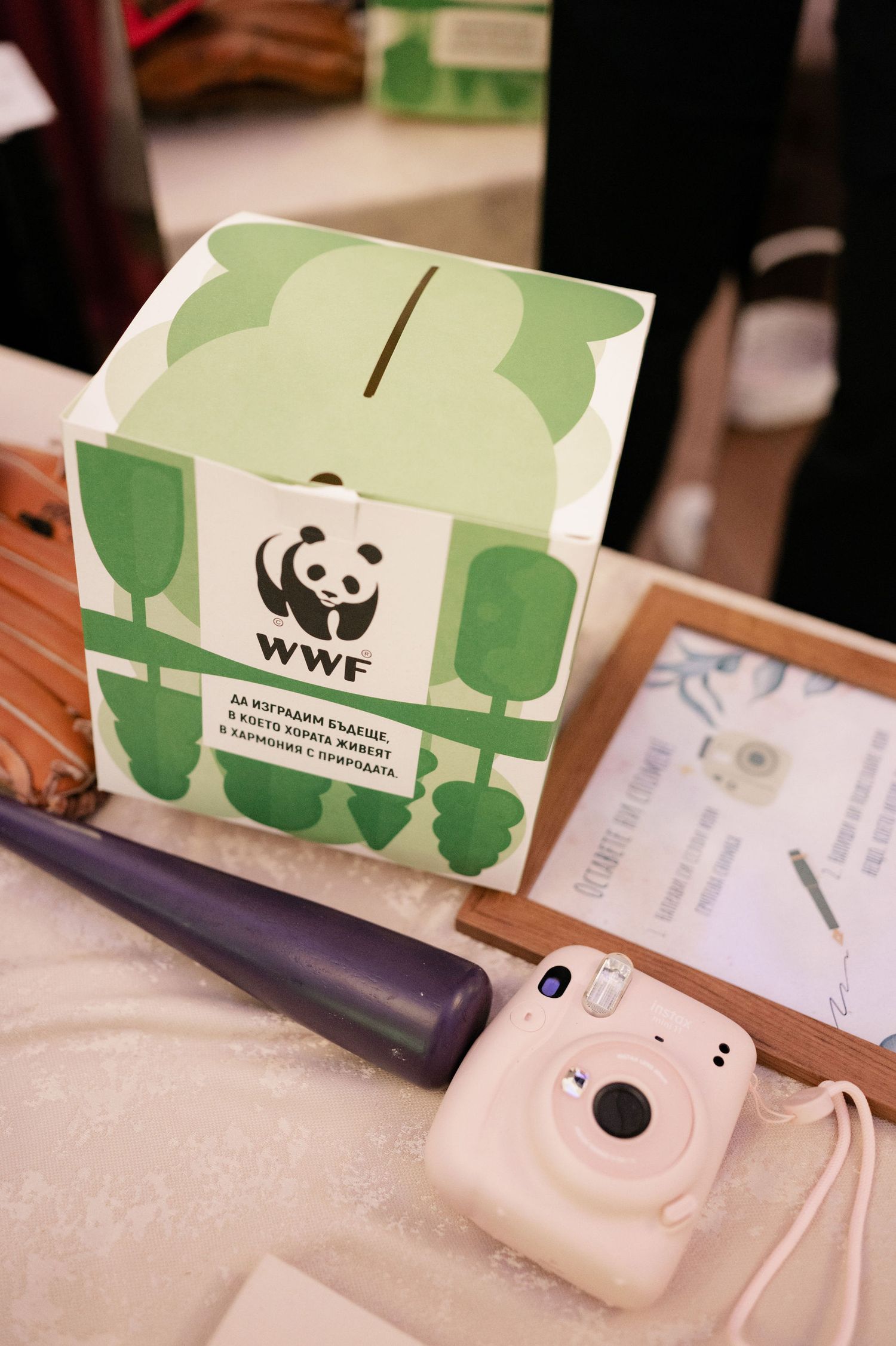 Green and white WWF panda logo donation box sits next to a white Polaroid-style camera on a light surface.