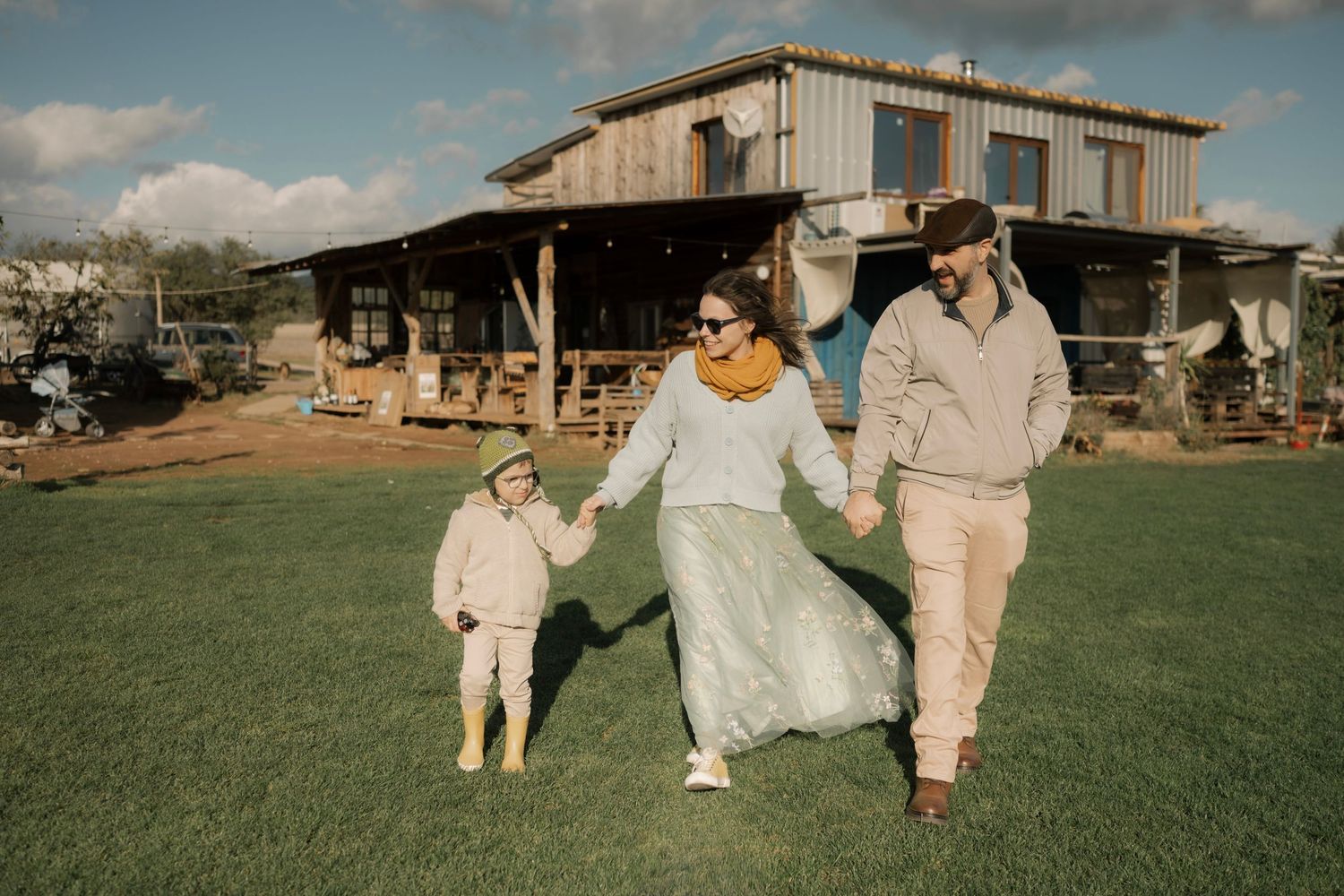 Wedding party in neutral outfits walks across a lush green lawn at a rustic outdoor venue during golden hour.