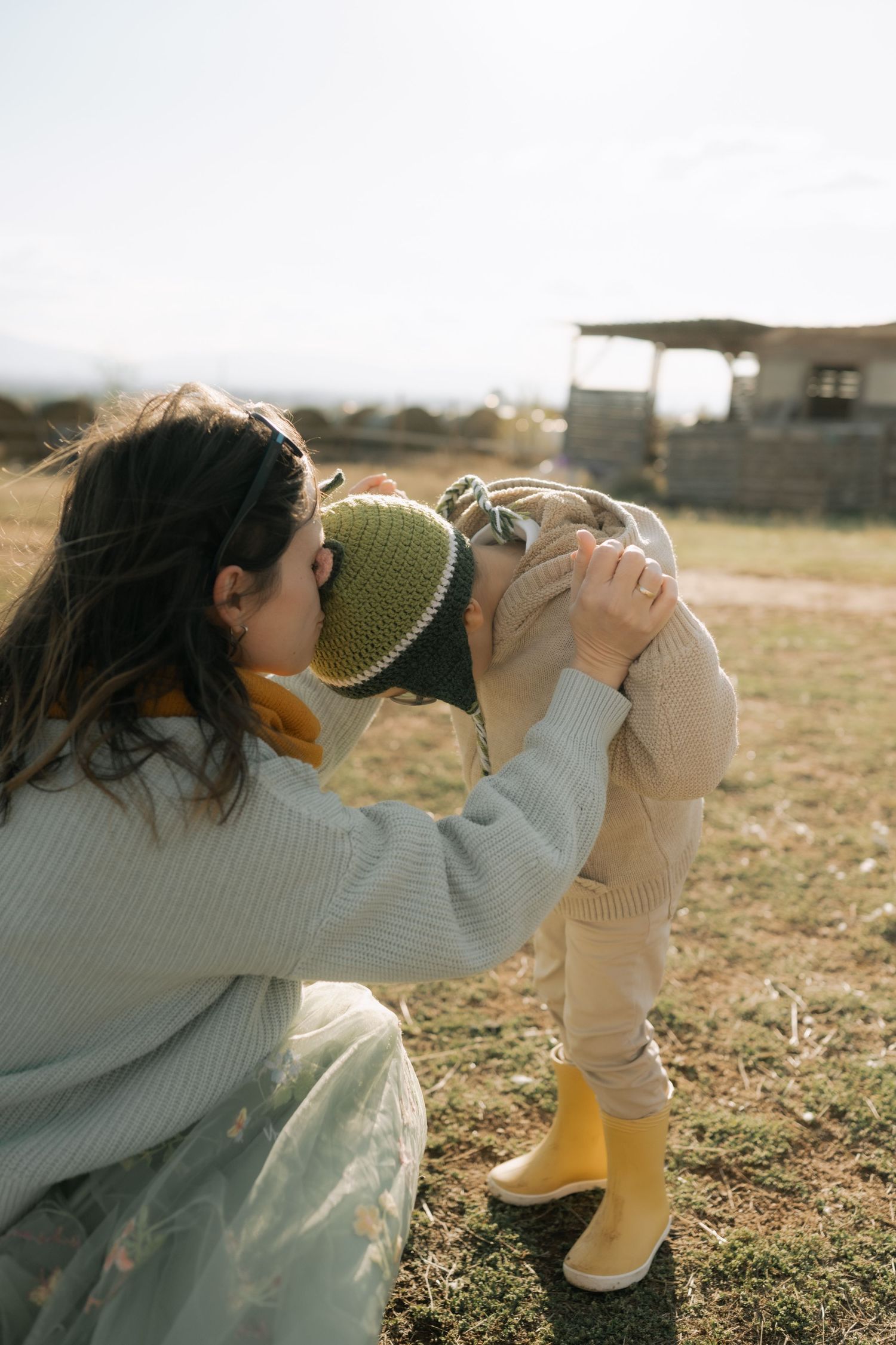 A person in a gray sweater takes photos with a vintage camera in a sunlit grassy field at golden hour.