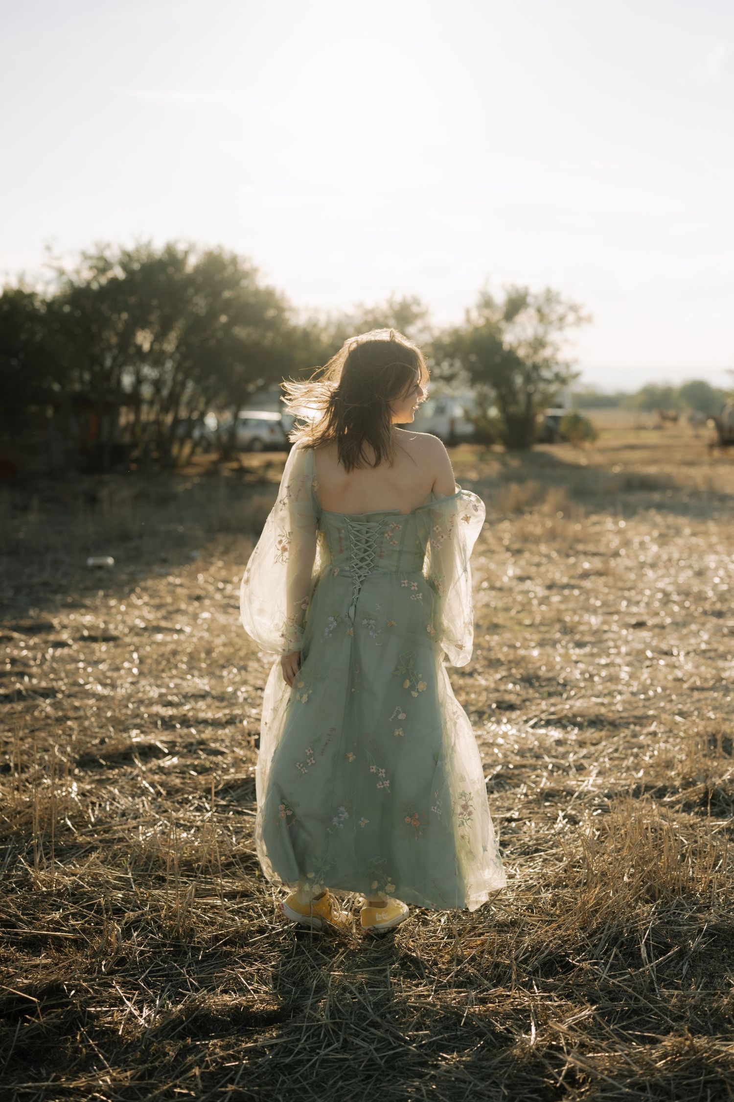 A person in a white vintage dress sits in a sun-drenched field during golden hour.